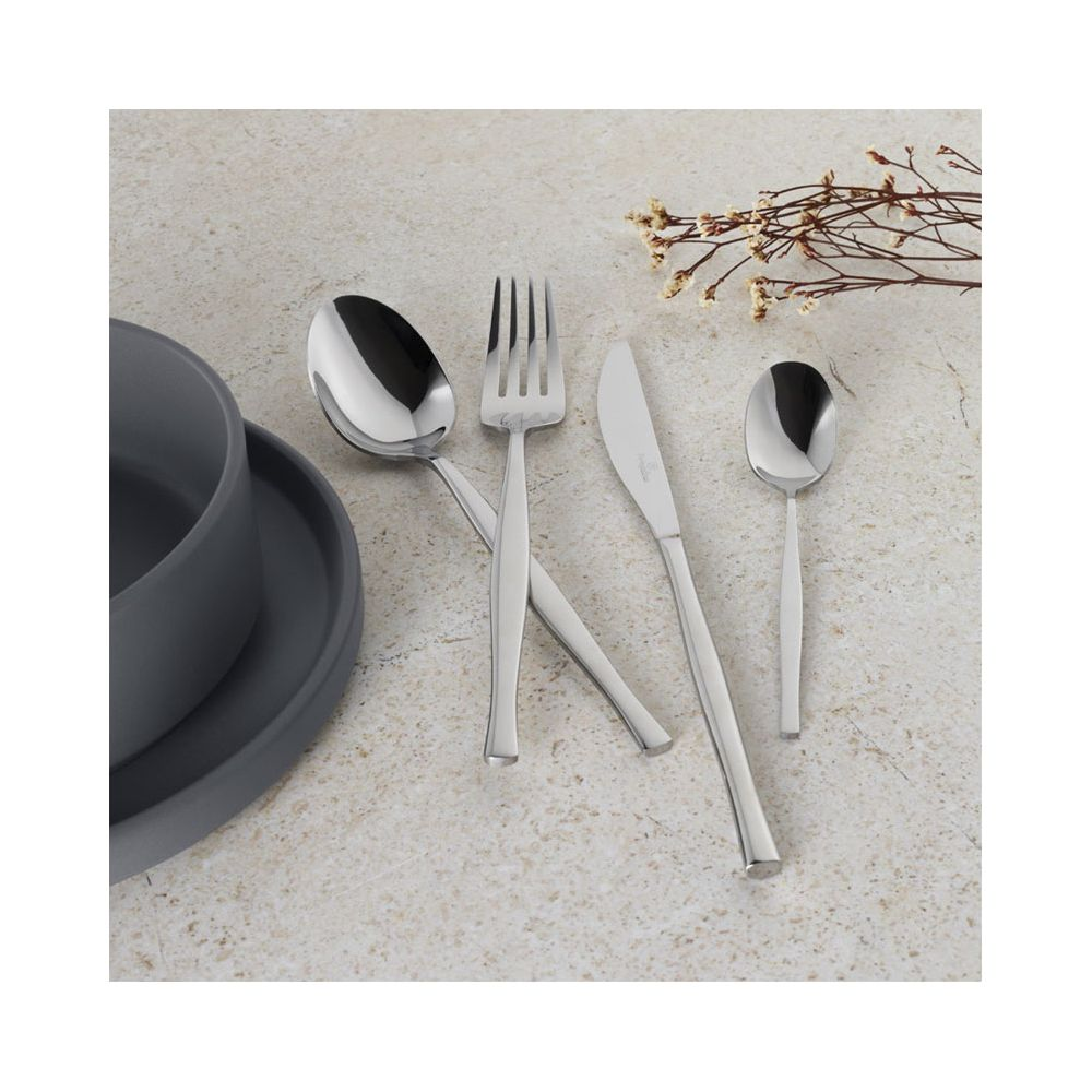Couverts en argent comprenant fourchette, cuillères et couteau sur une table texturée près d'un bol foncé.