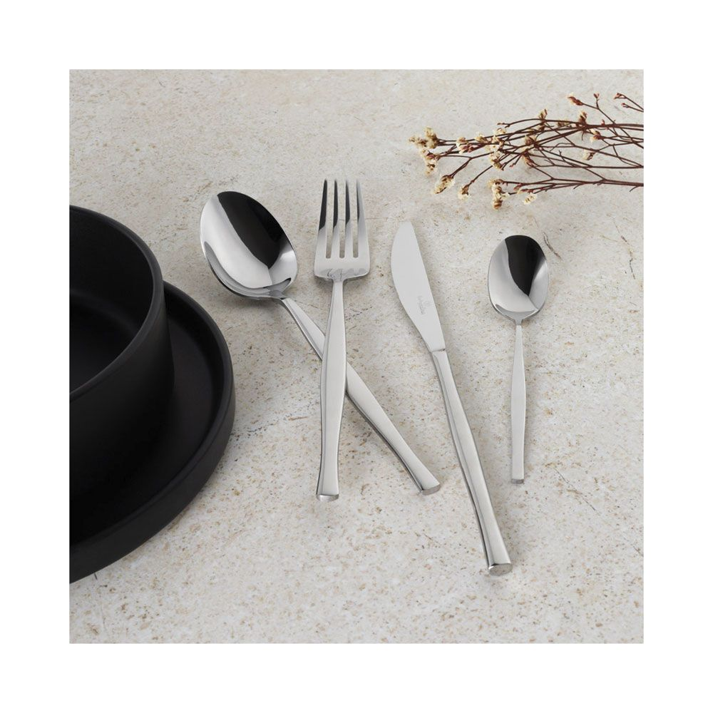 Couverts brillants avec cuillère, fourchette, couteau et petite cuillère près d'un bol noir sur pierre claire.
