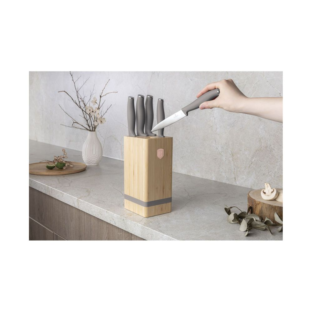 Une main retire un couteau à manche gris d'un bloc en bois sur un comptoir.