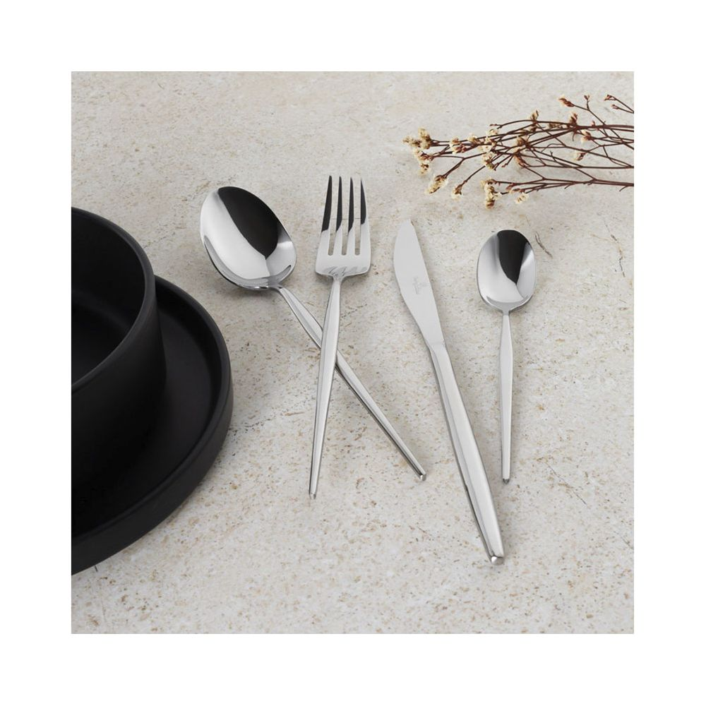 Couverts en acier inoxydable avec cuillère, fourchette, couteau et petite cuillère près d'un bol noir sur table.