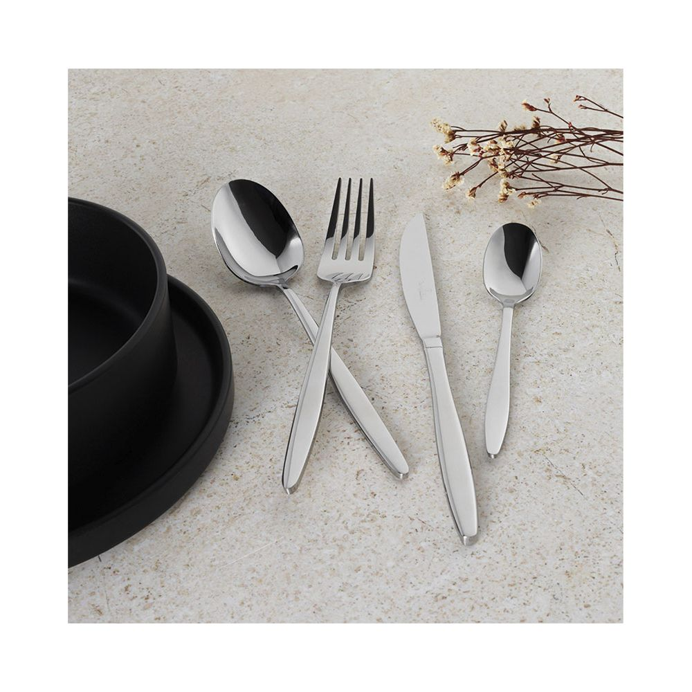 Des couverts en argent avec cuillère, fourchette, couteau et petite cuillère près d'un bol noir sur une table claire.
