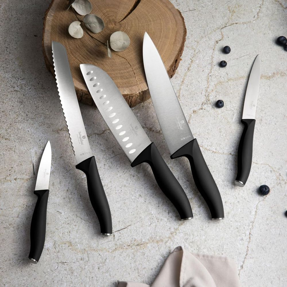 Fünf Küchenmesser mit schwarzen Griffen und silbernen Klingen auf einer Marmoroberfläche mit Blaubeeren und Holz.