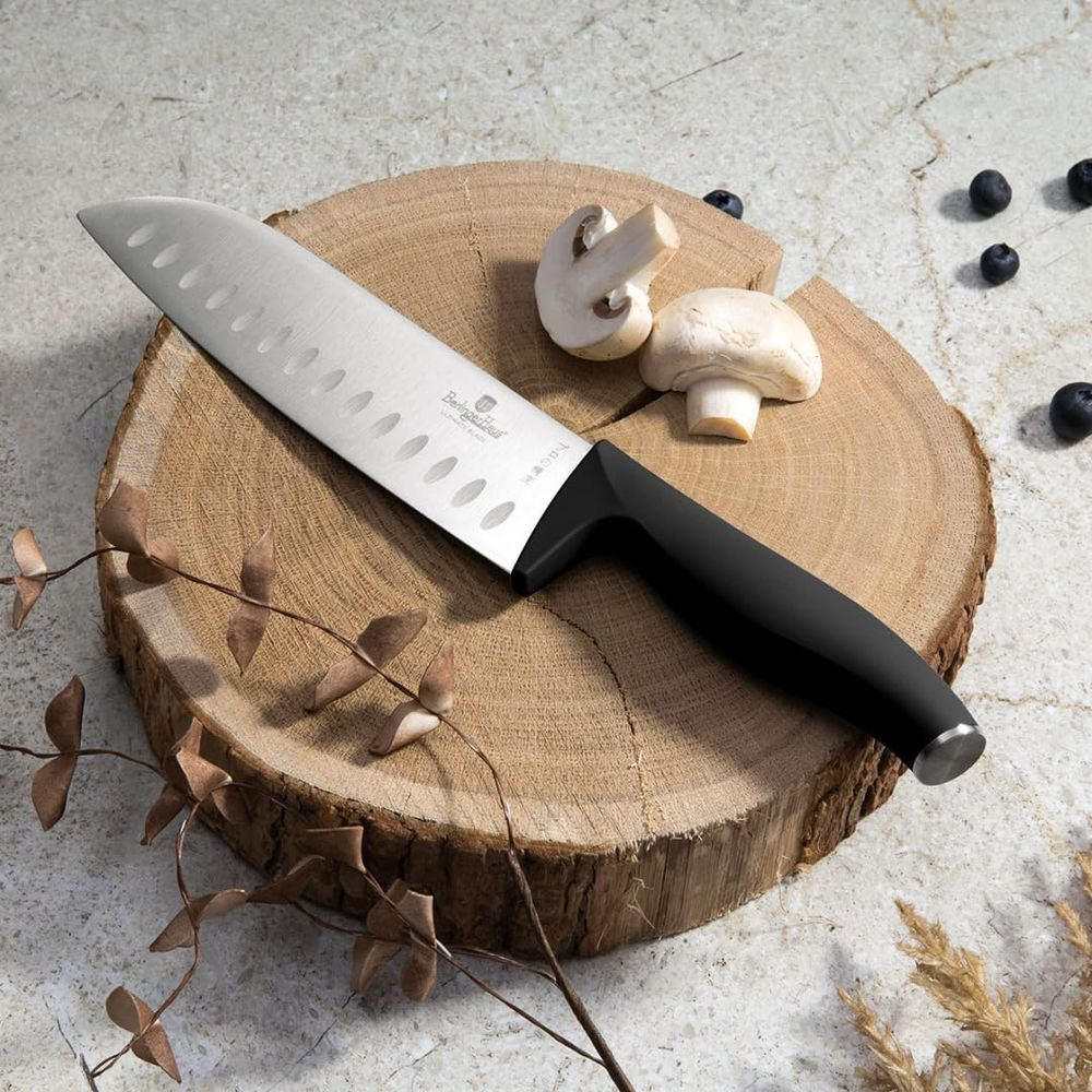 Ein Santokumesser mit schwarzem Griff liegt auf einem Holzbrett neben Pilzen und Blaubeeren.