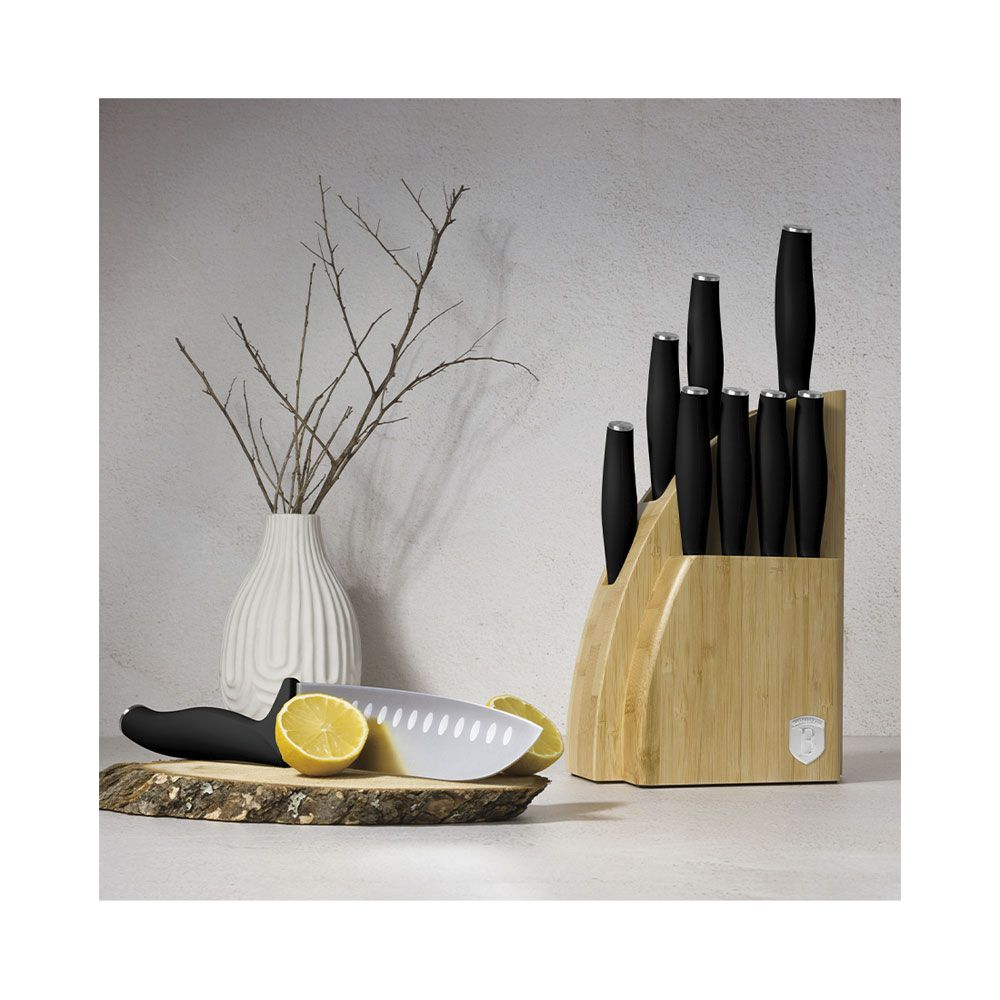 Un bloc à couteaux en bois, un citron coupé sur une planche et un vase blanc avec des branches.