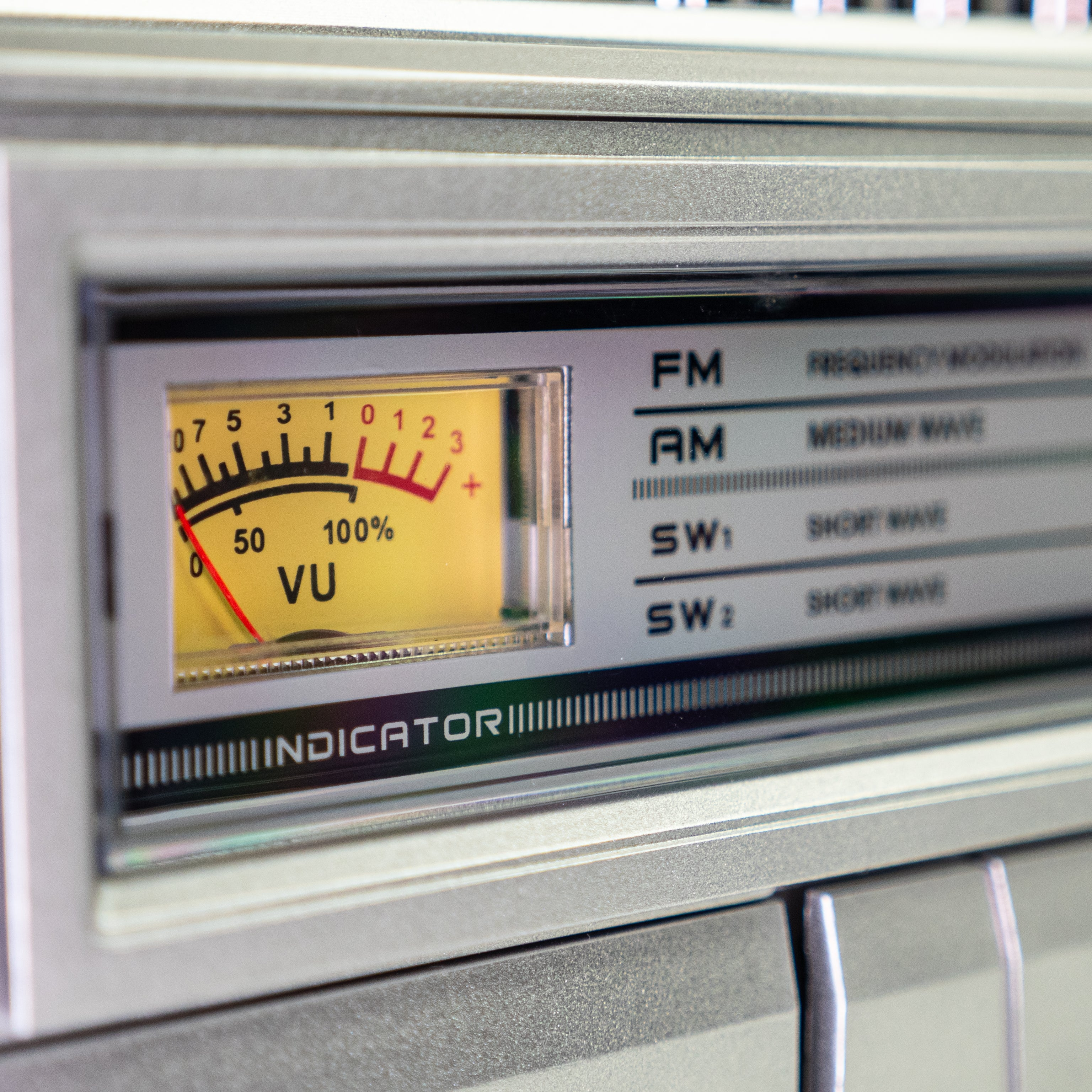 Nahaufnahme einer analogen VU-Meter-Anzeige an einem silbernen Audiogerät mit FM- und AM-Skala.