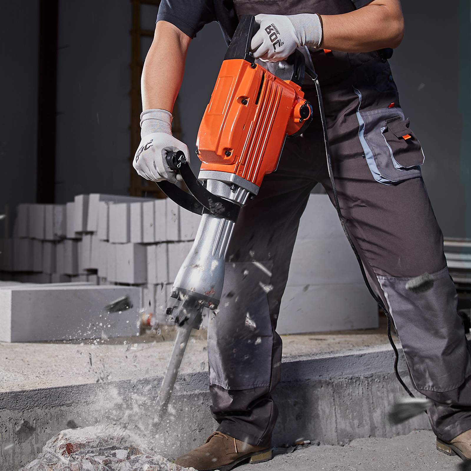 Un trabajador con ropa de trabajo gris usa un martillo neumático naranja y plateado para romper hormigón.