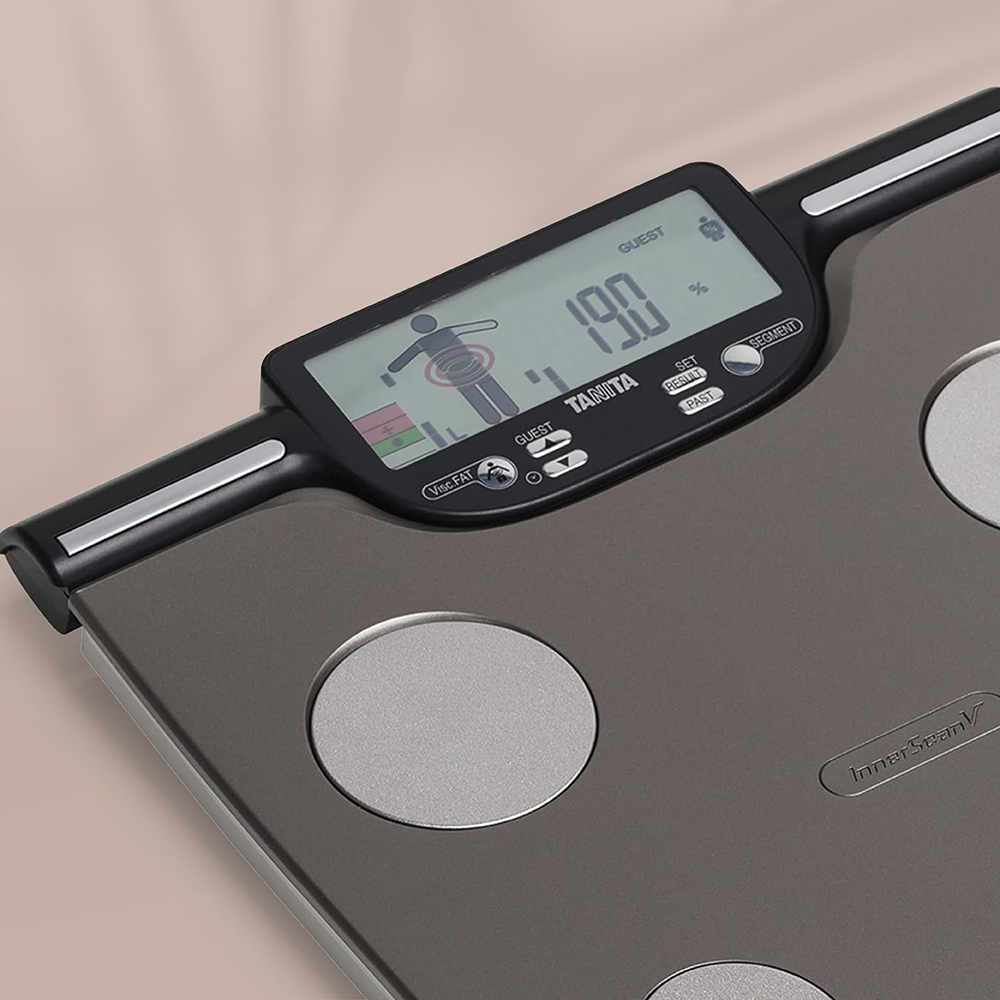 Gros plan sur un pèse-personne numérique Tanita gris foncé avec des électrodes circulaires argentées et un écran LCD.