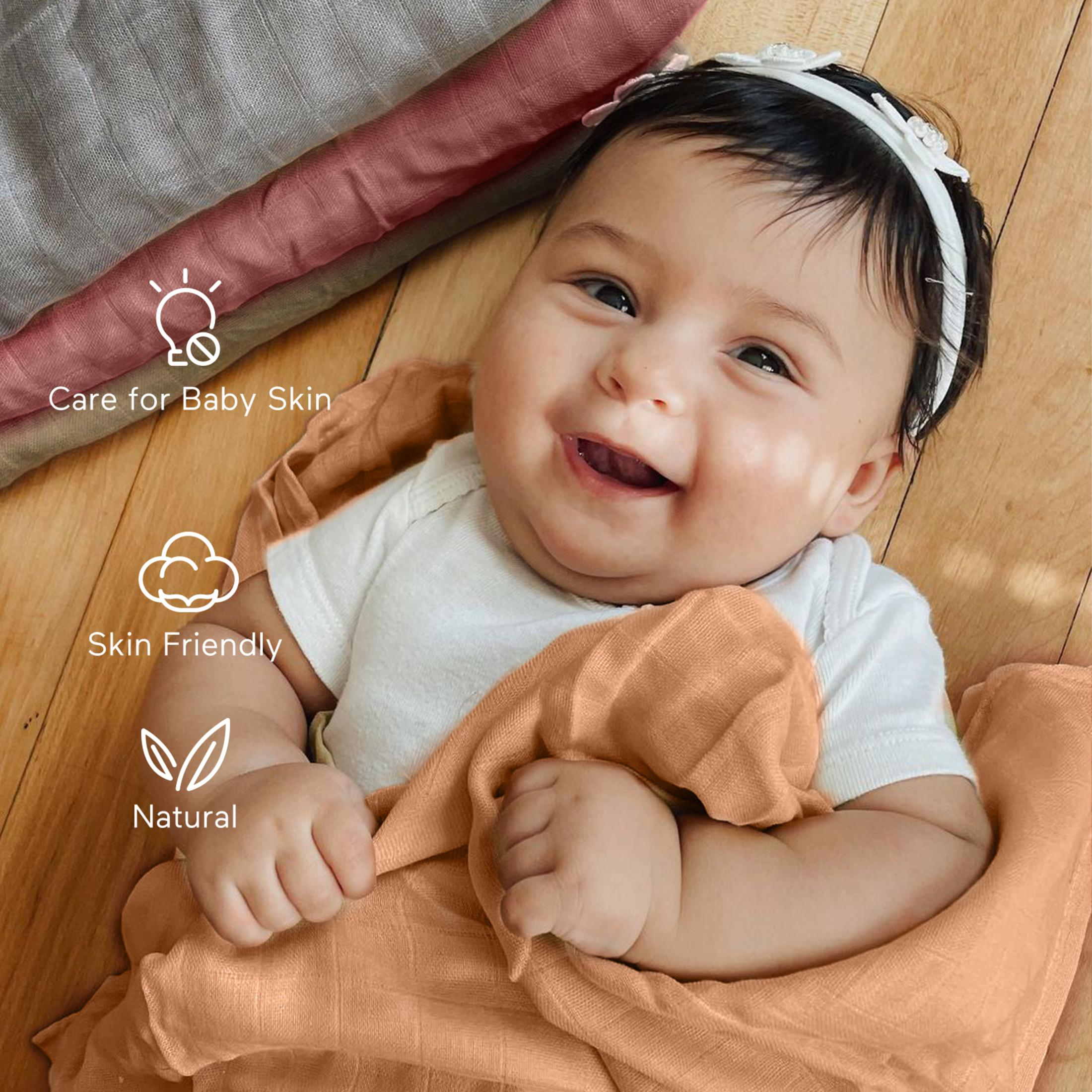 Bebè sorridente in camicia bianca con fascia, circondato da coperte su legno.