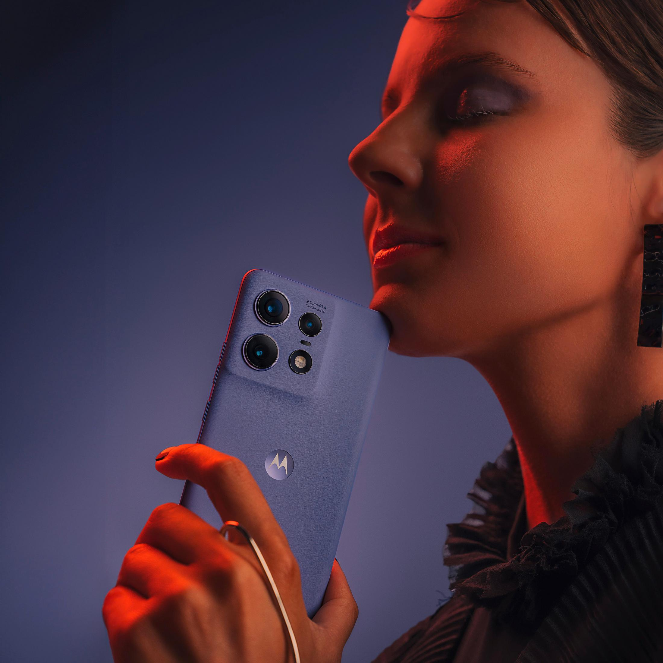 Eine Frau hält ein blaues Smartphone mit Mehrfachkamera vor ihr Gesicht im roten Licht.