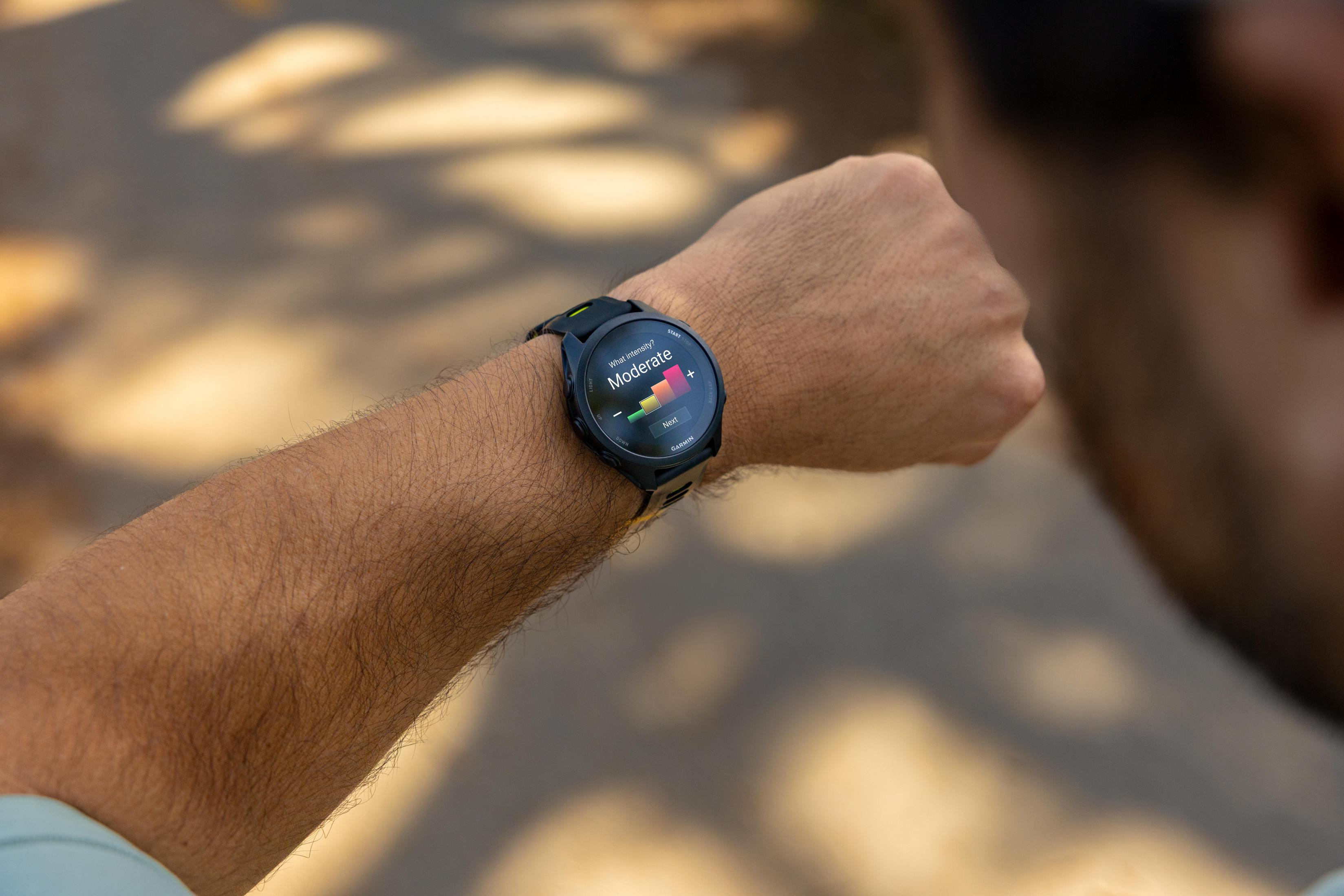 Una persona guarda uno smartwatch che mostra un grafico di intensità moderata su un sentiero soleggiato.