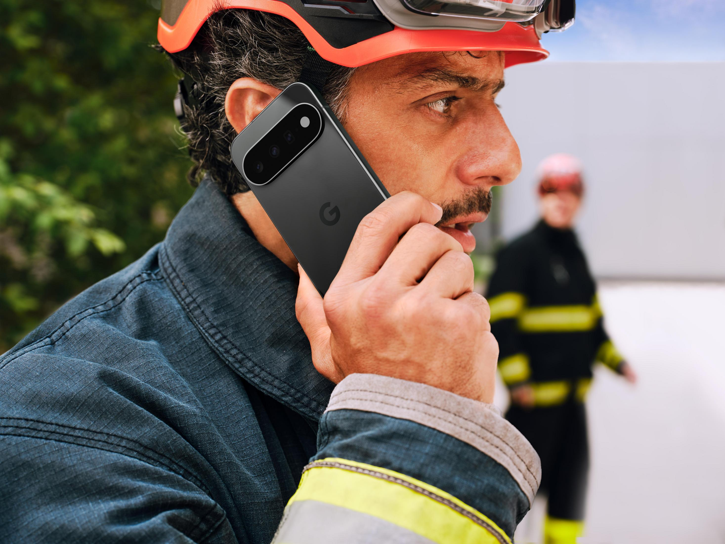 Strazak w helmie rozmawia przez czarny smartfon na zewnatrz.