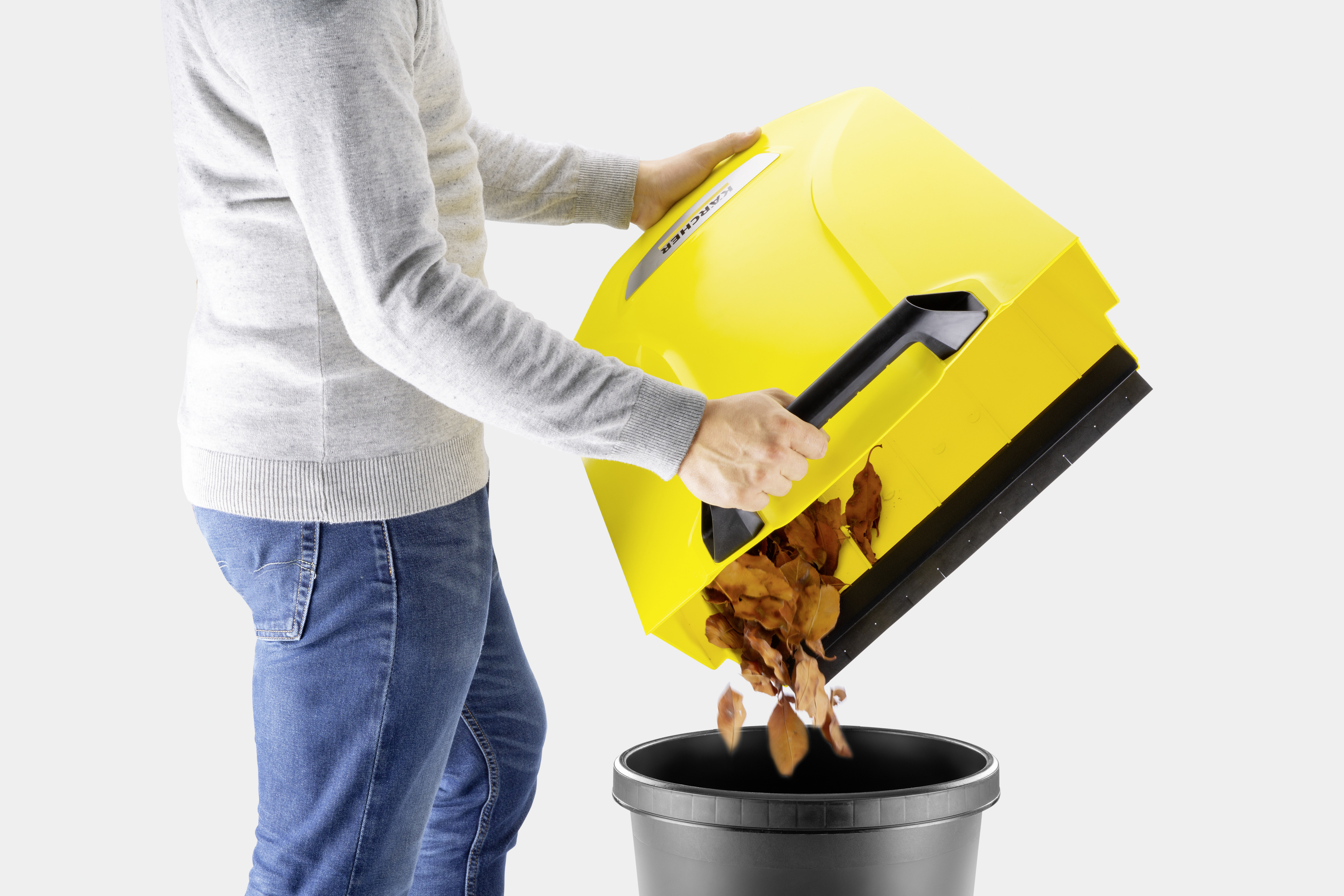 Persona vaciando un recolector de hojas amarillo en un cubo negro.