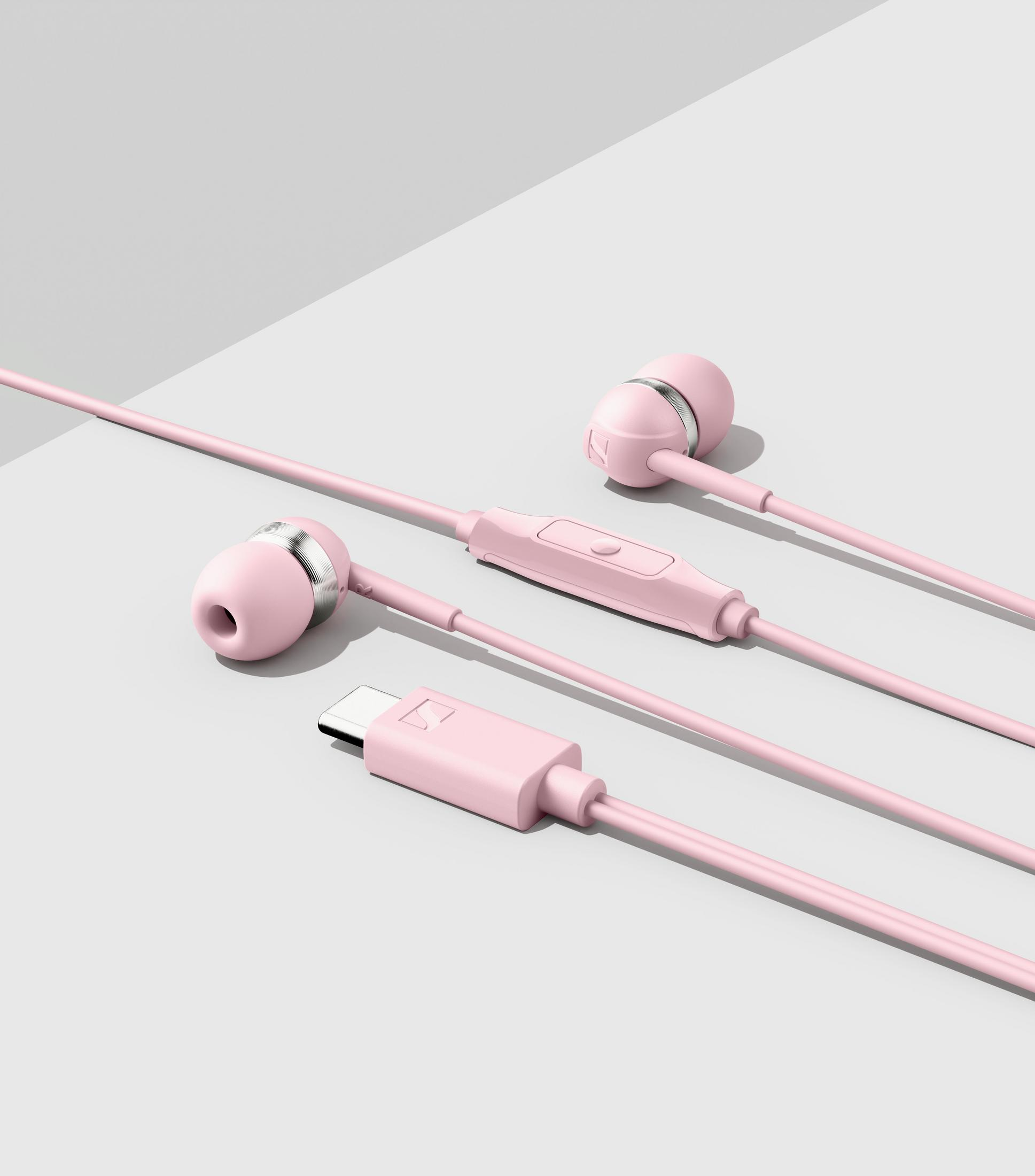 Auriculares con cable rosa con control en línea y conector USB-C sobre superficie gris.