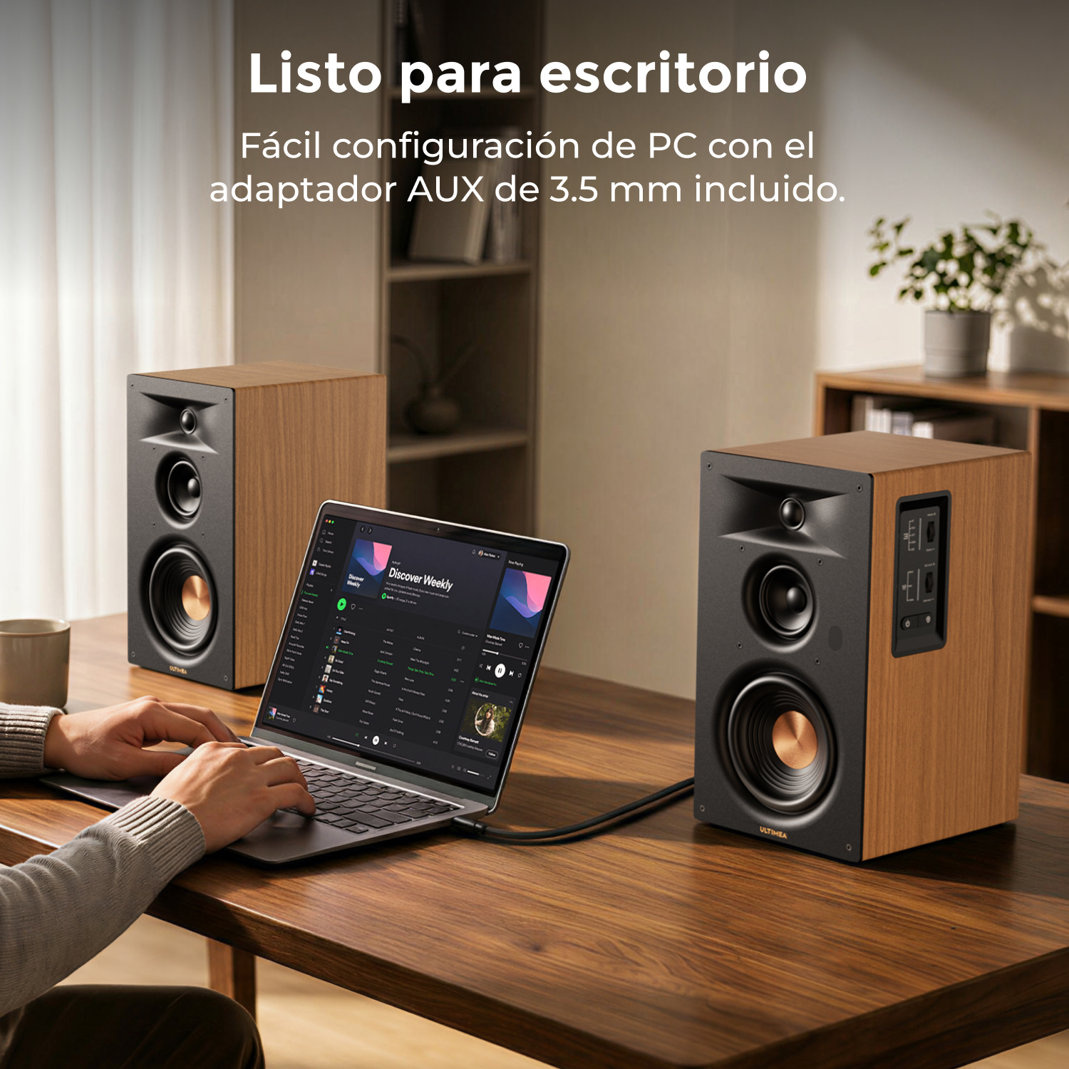 Persona escribiendo en portátil en escritorio con dos altavoces.