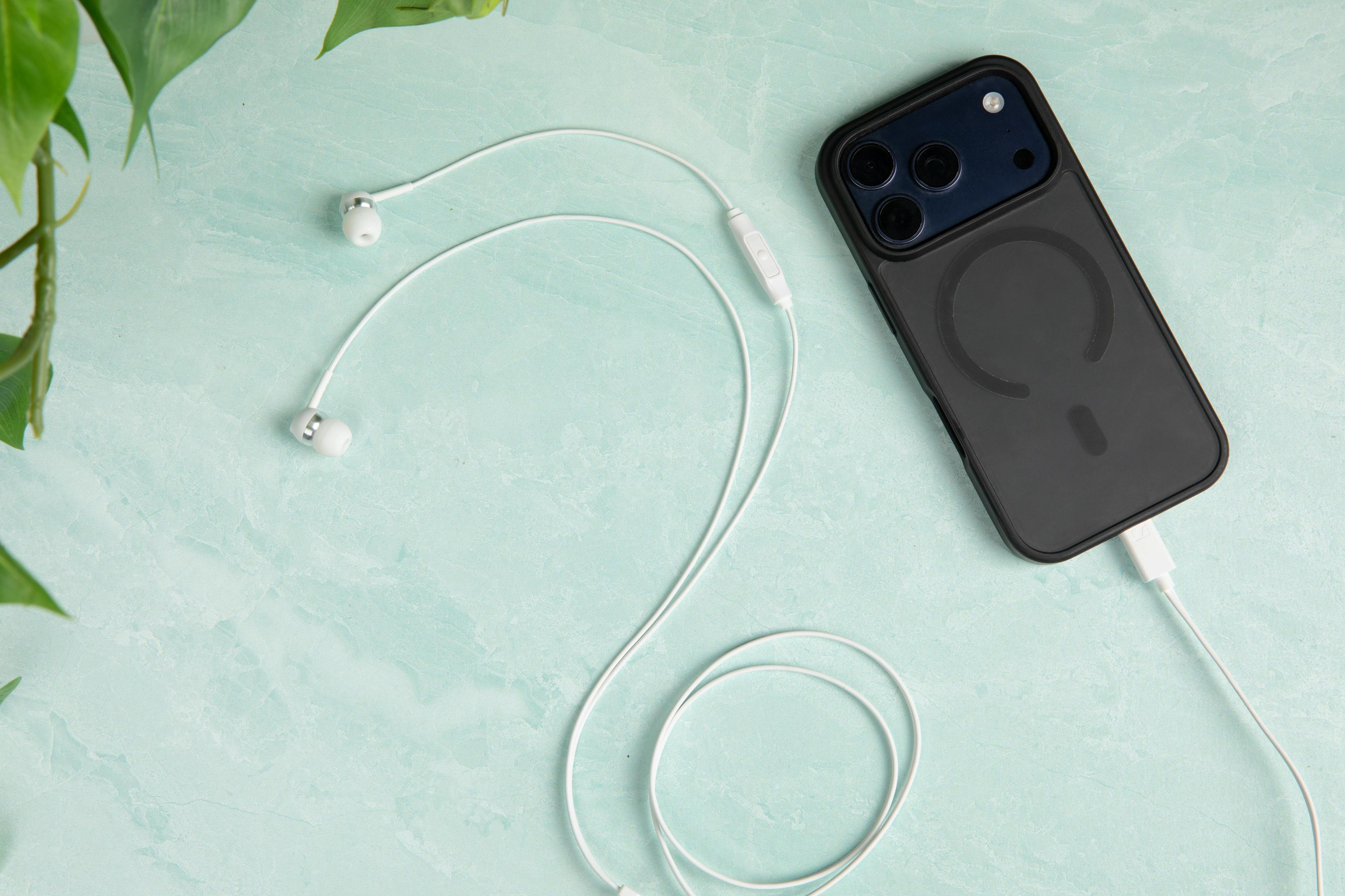 Un teléfono inteligente en funda protectora con auriculares conectados sobre fondo verde.