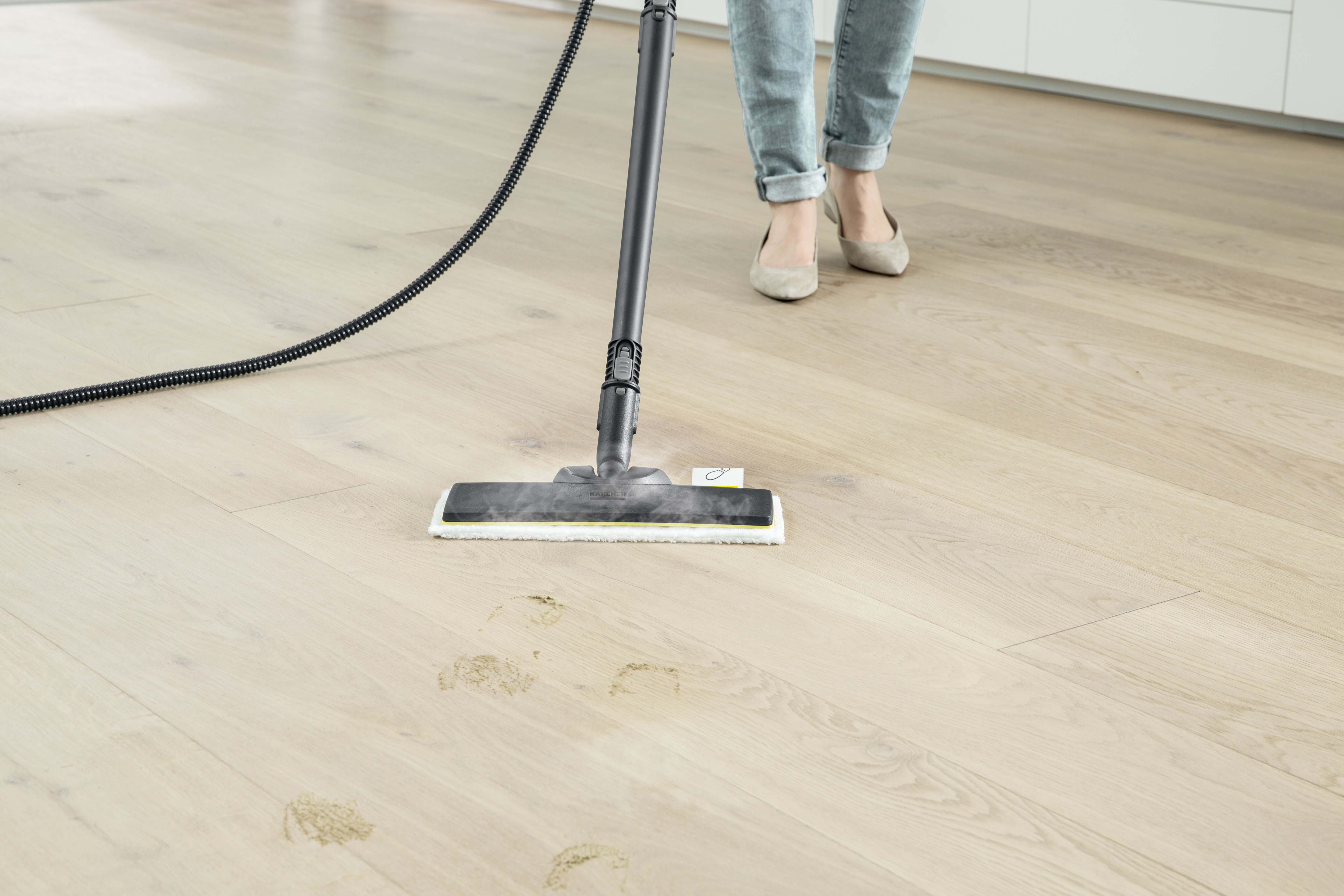 Iemand reinigt een houten vloer met een stoomreiniger en verwijdert vuilvlekken.
