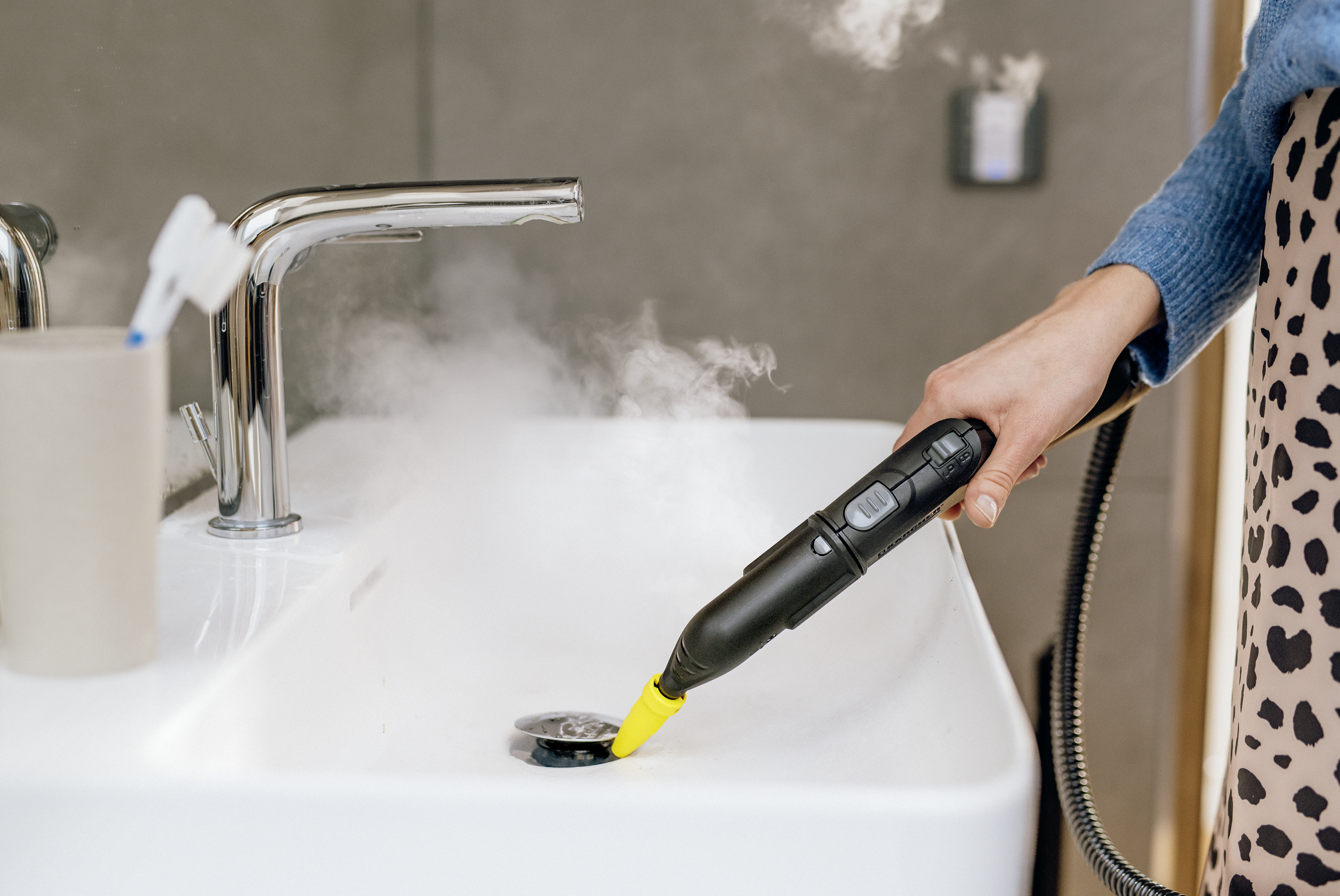 Una persona usa un limpiador a vapor portátil para desinfectar un lavabo blanco.