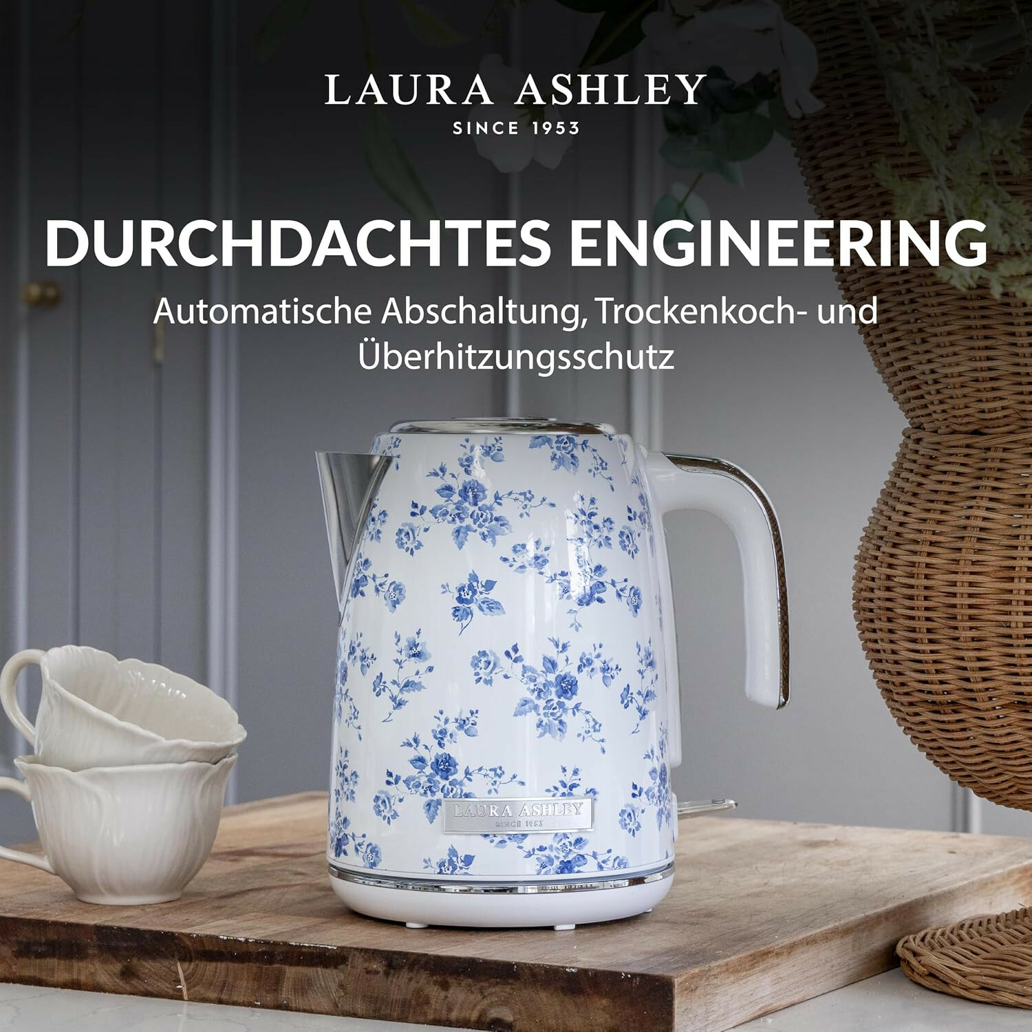 Bollitore Laura Ashley con motivo floreale blu su asse di legno, vicino a due tazze bianche.