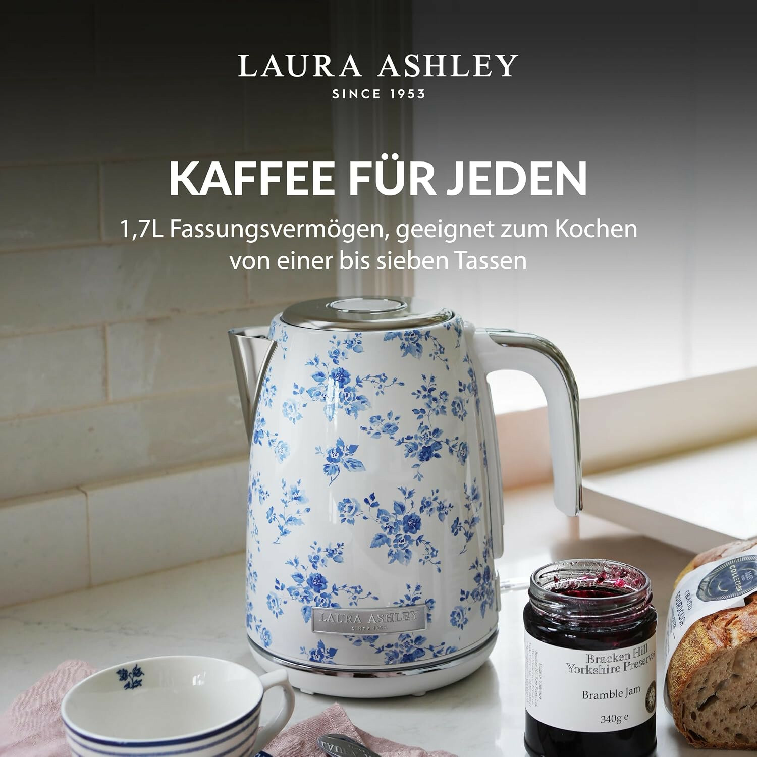 Bollitore Laura Ashley con motivo floreale blu su un piano cucina accanto a una tazza, marmellata e pane.