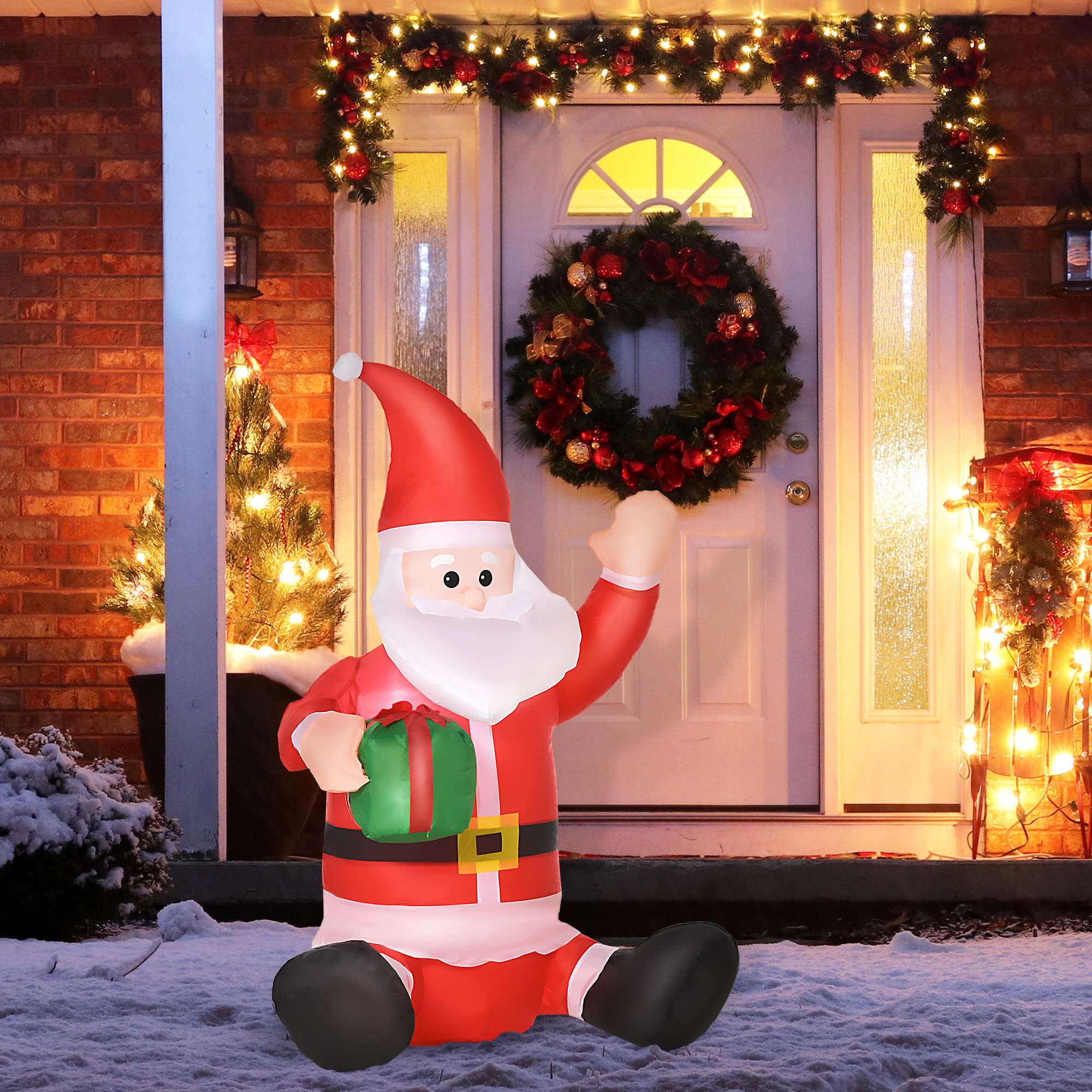 Un Papá Noel inflable con un regalo sentado en la nieve frente a una puerta decorada.