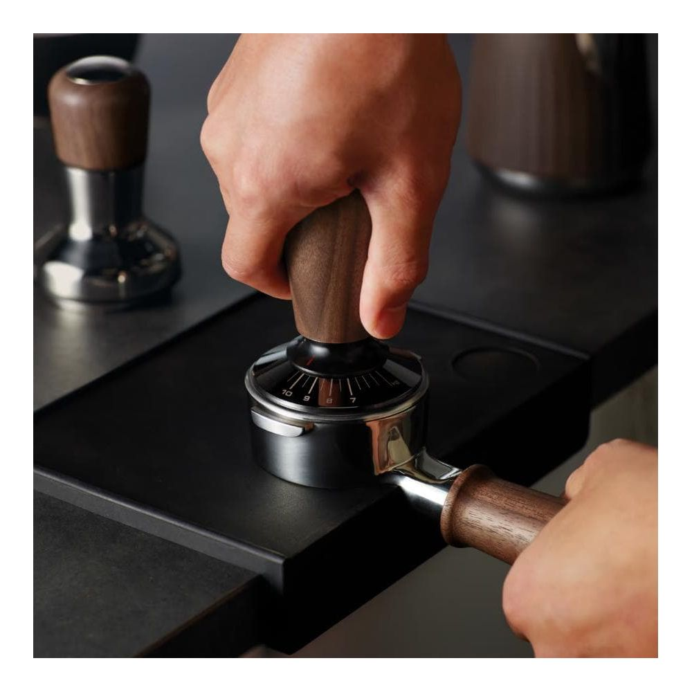 Eine Hand hält einen Holz-Kaffee-Tamper, um Kaffeepulver in Siebträger zu pressen.