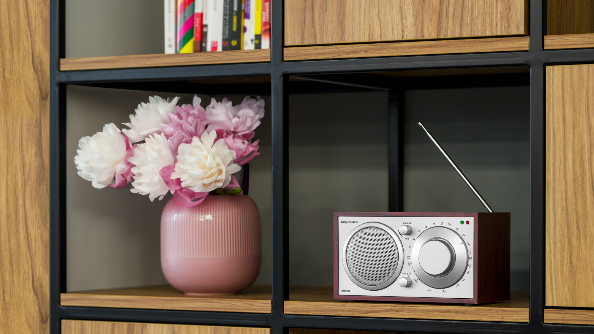 Radio w stylu retro stoi na półce obok różowego wazonu z kwiatami.