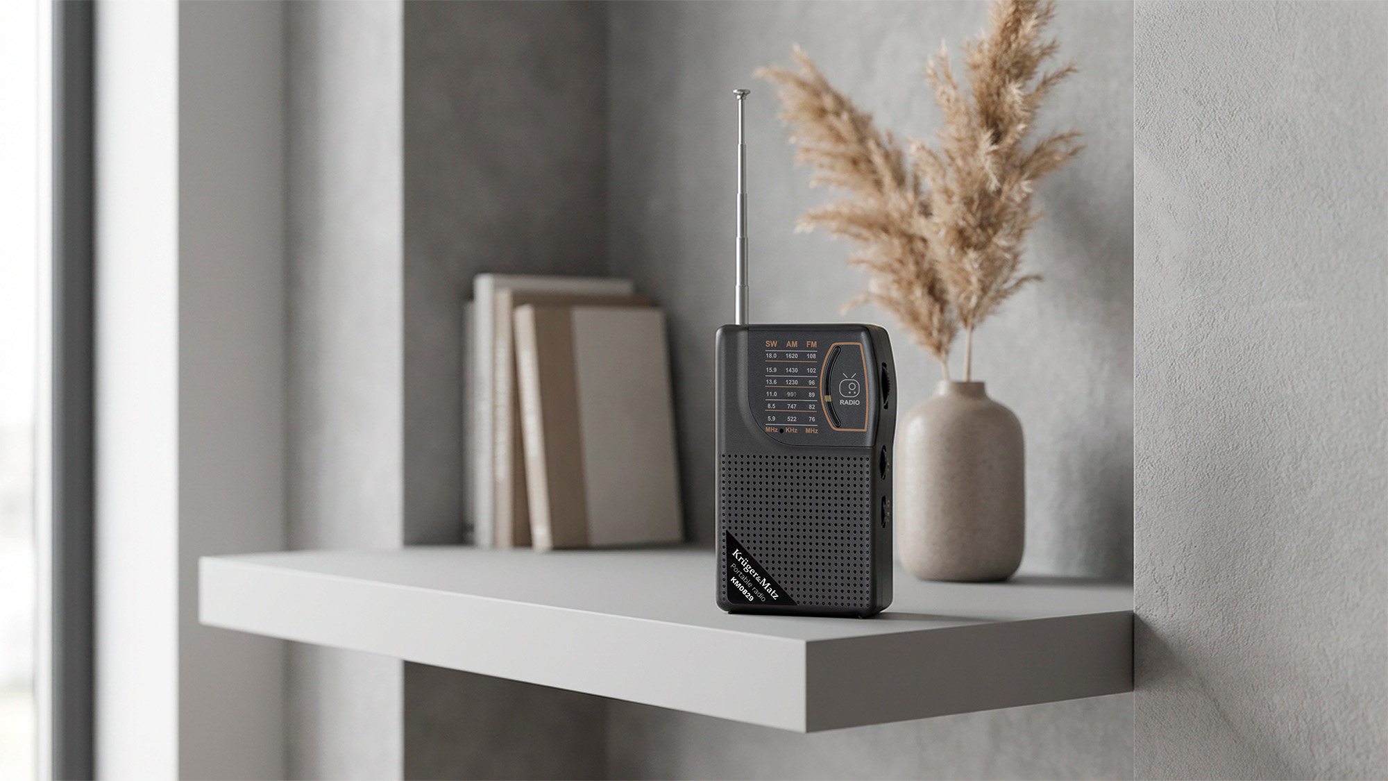 Przenośne szare radio stoi na szarej półce obok ułożonych książek i wazonu z suszonymi kwiatami.