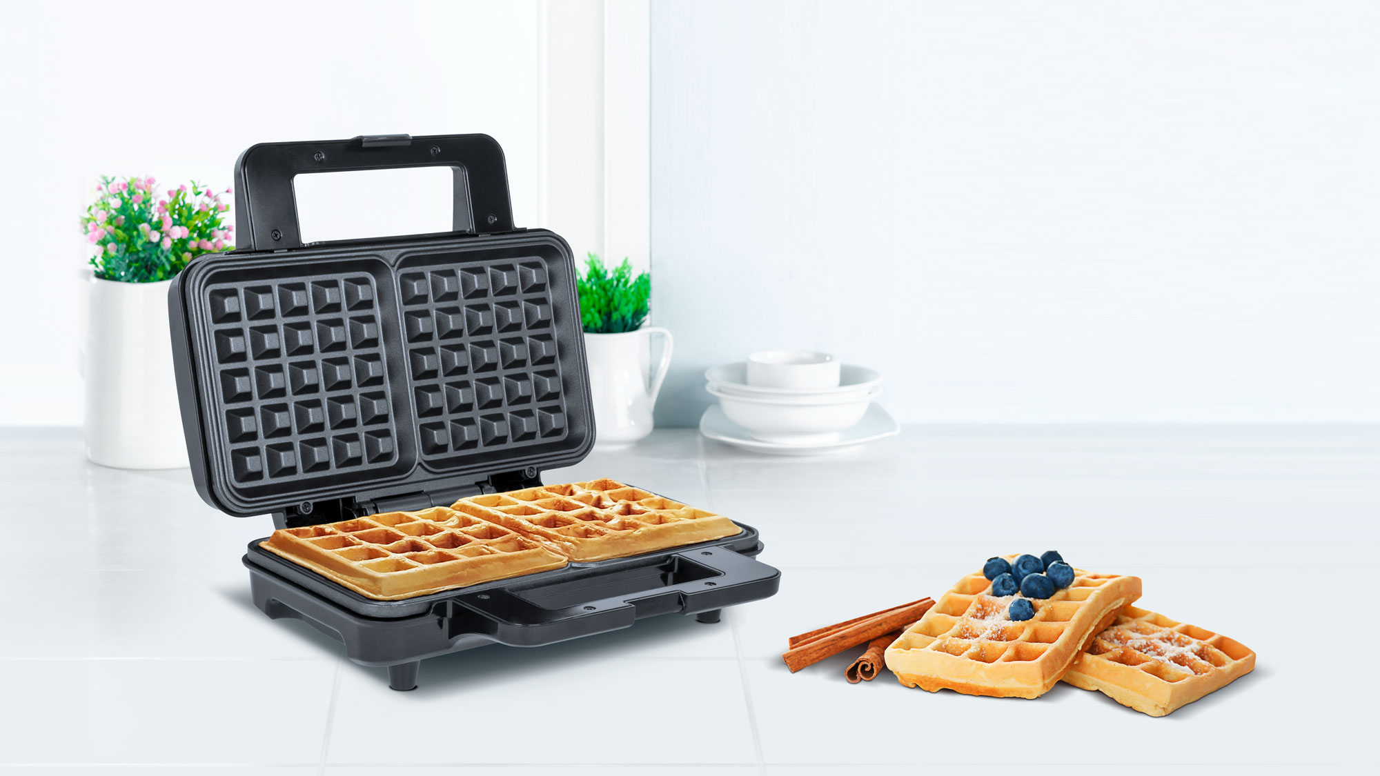 Otwarta gofrownica na blacie kuchennym ze świeżymi goframi i borówkami obok.