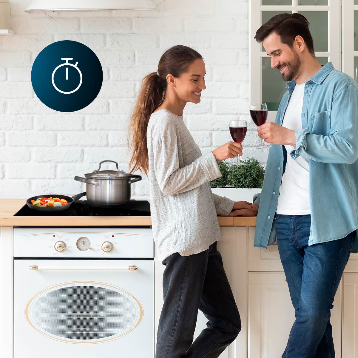 Una pareja feliz en la cocina brinda con vino tinto mientras se cocinan verduras.