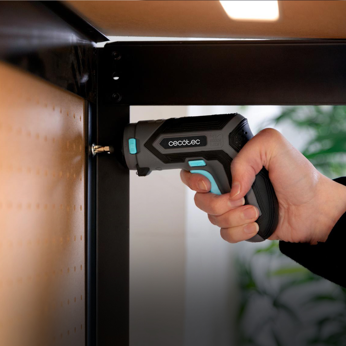Una mano tiene un avvitatore a batteria grigio con dettagli blu, inserendo una vite in una struttura in metallo nero.