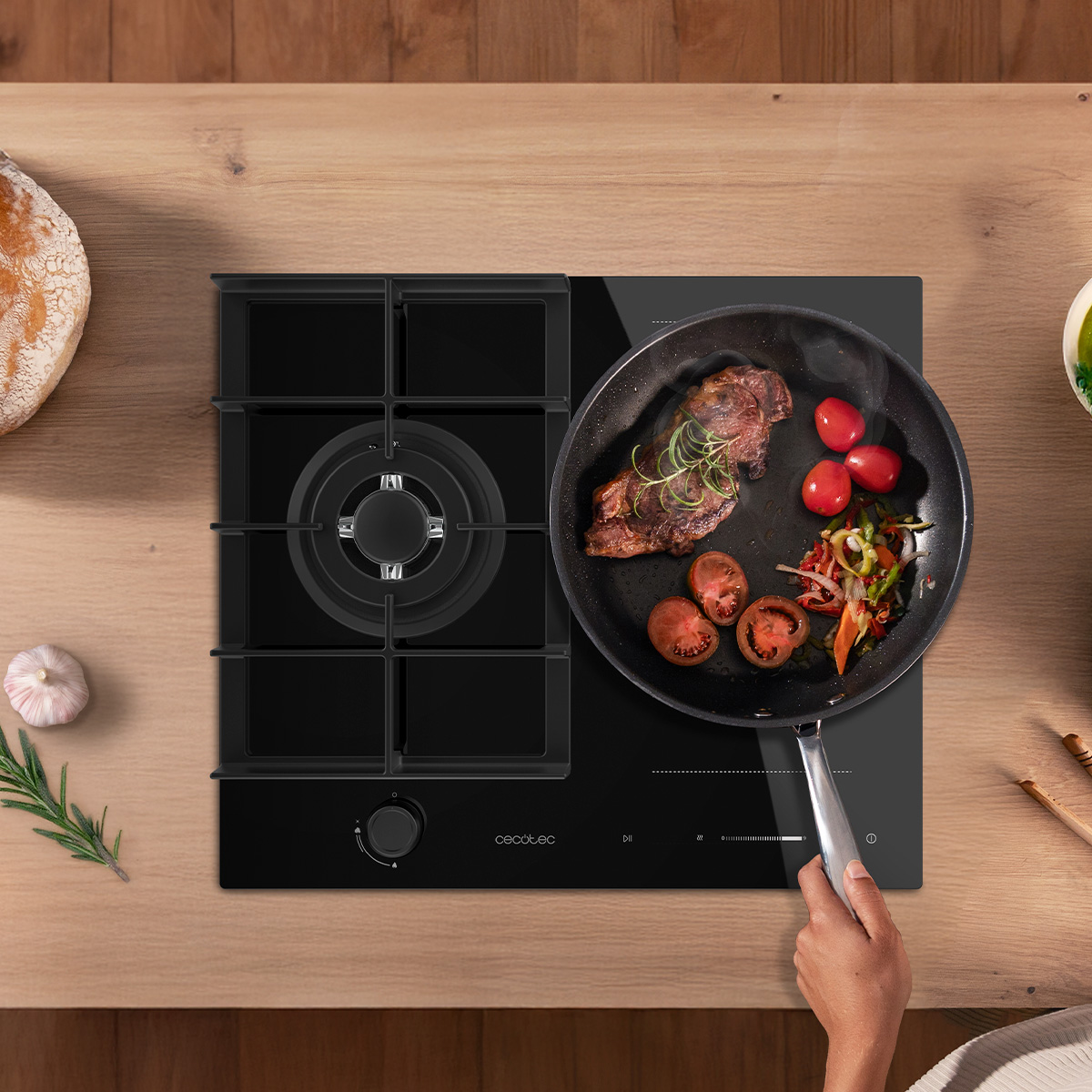 Una mano sostiene una sartén en una estufa con carne, tomates y hierbas, en una mesa de madera.