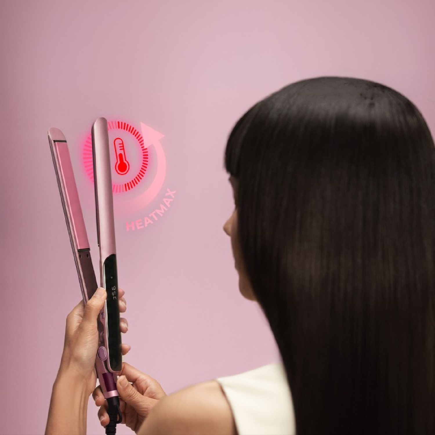 Una donna tiene una piastra per capelli rosa con un'icona di calore digitale vicina.