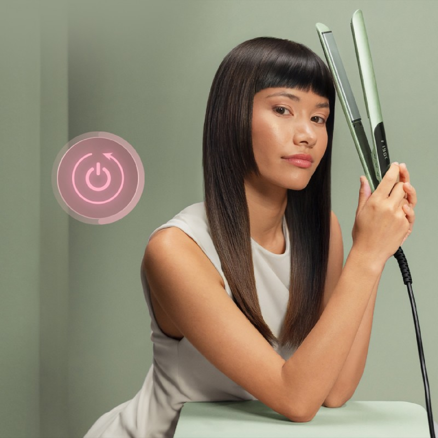 Una donna con capelli scuri e lisci tiene in mano una piastra per capelli verde chiaro.