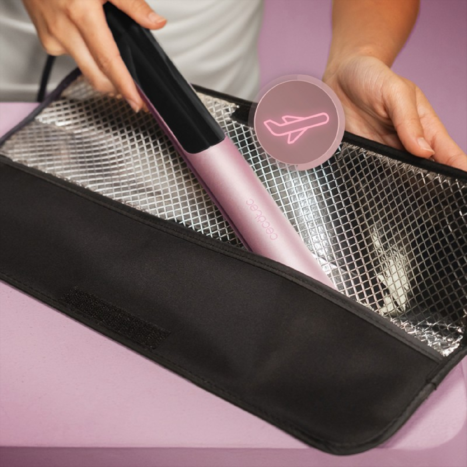 Una persona ripone una piastra per capelli rosa in una borsa nera con fodera interna riflettente argentata.