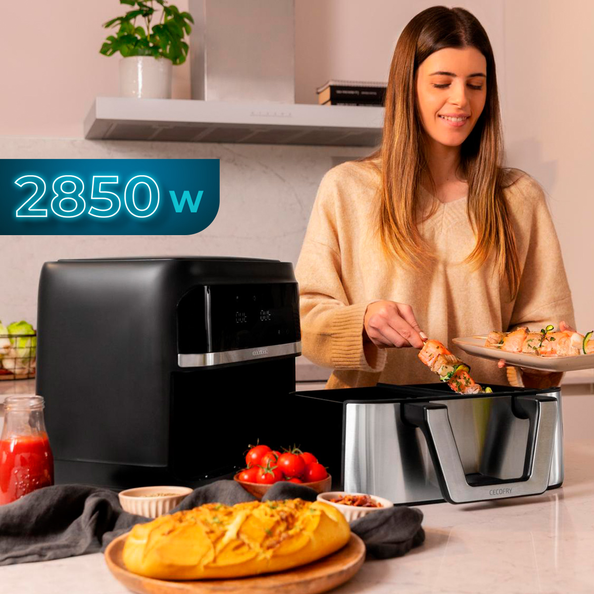 Una mujer en una cocina sostiene brochetas junto a una freidora de aire negra. Hay tomates y pan en el mostrador.