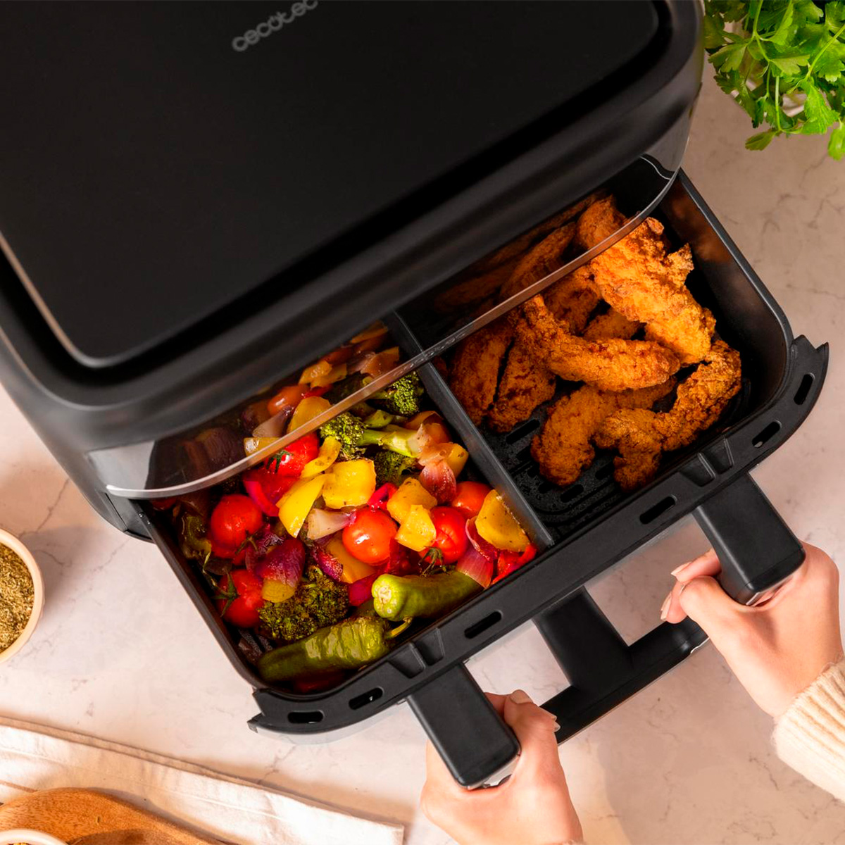 Se abre una freidora de aire de doble compartimento con pollo frito y verduras mixtas coloridas.