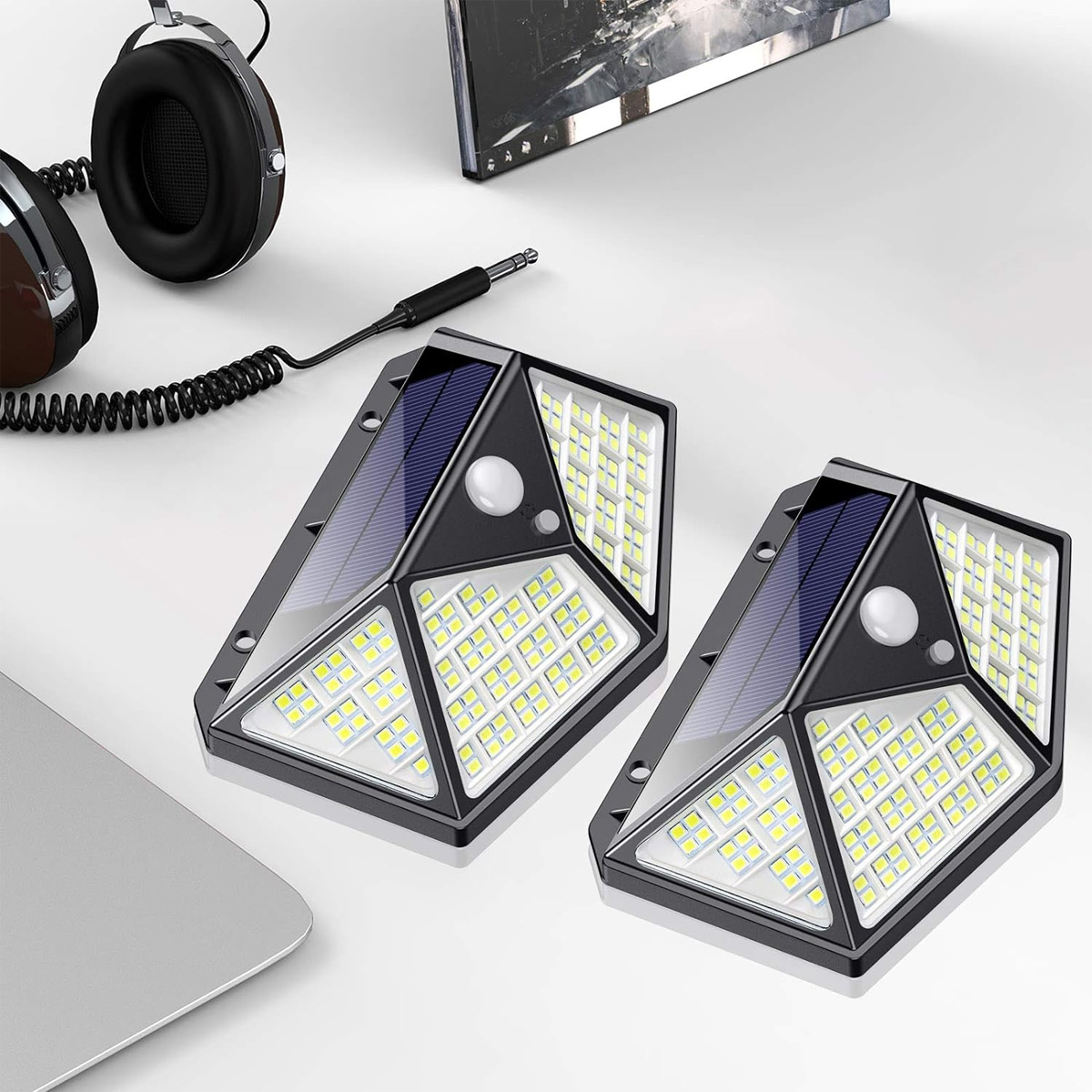 Zwei solarbetriebene LED-Wandleuchten mit Bewegungsmeldern liegen auf einem weißen Schreibtisch.