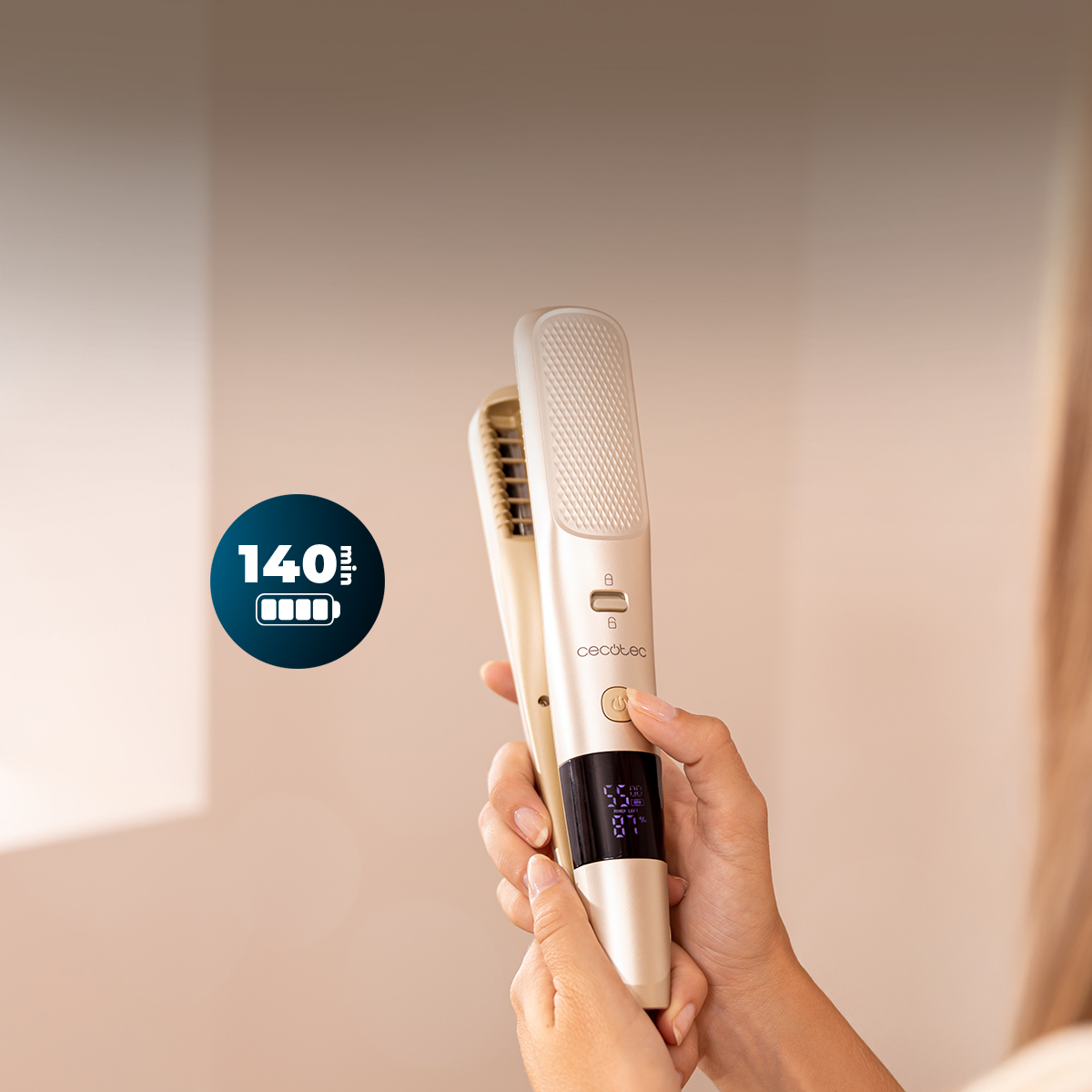 Una mano sostiene una plancha de pelo dorada Cecotec con pantalla digital y 140 minutos de batería.