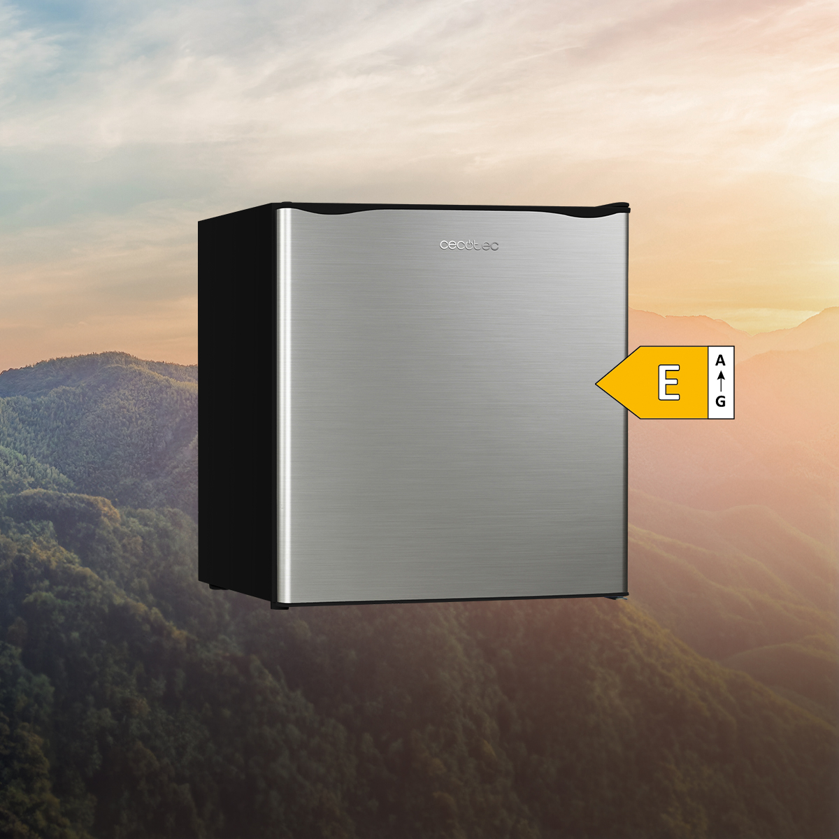 Un minifrigorífico plateado frente a un paisaje montañoso al atardecer, con etiqueta energética E.