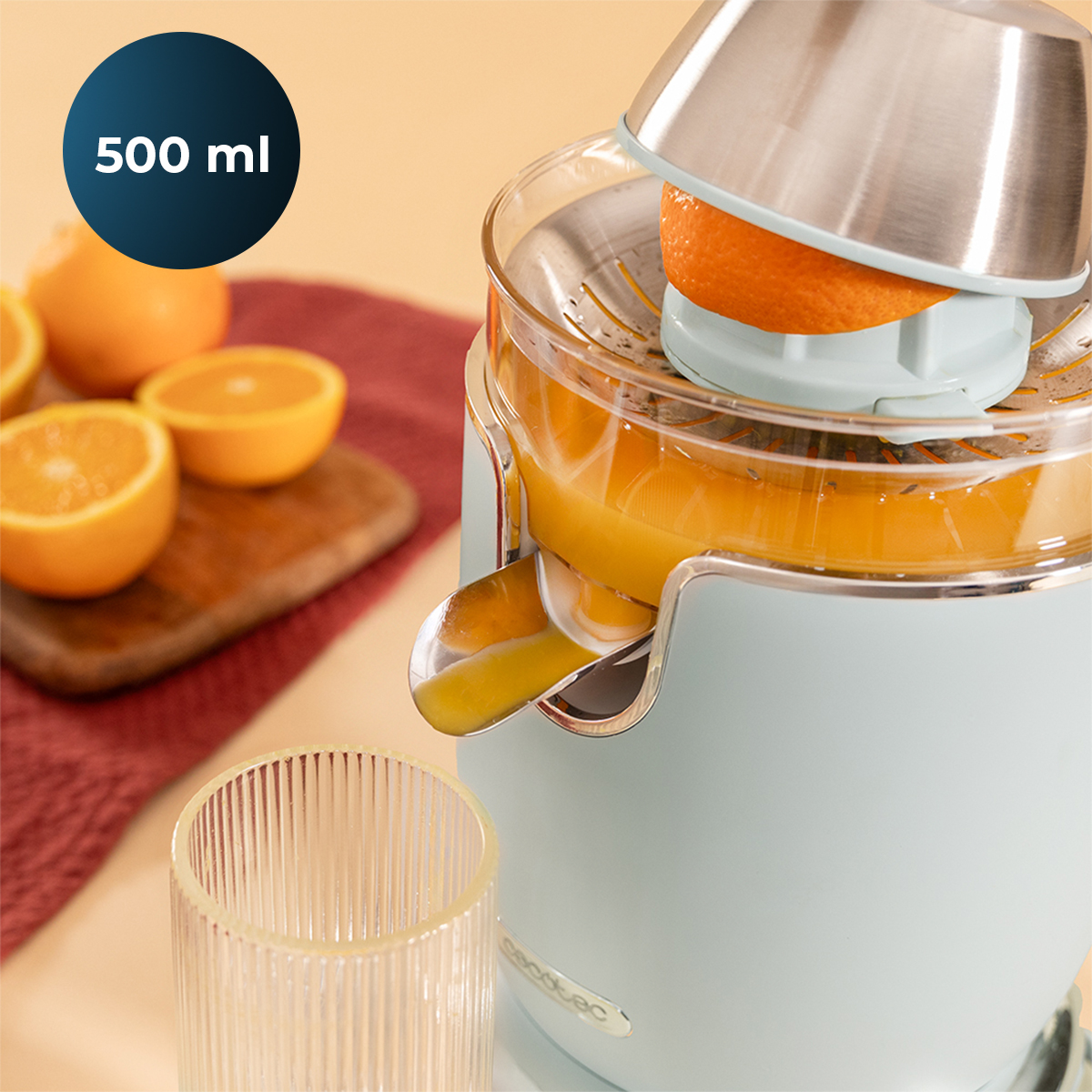 Un spremiagrumi elettrico azzurro spreme un'arancia, versando succo fresco in un bicchiere, con altre arance su un tagliere.