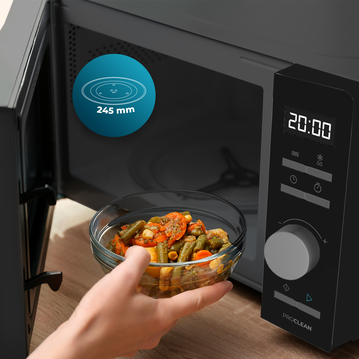 Mano sostiene un bol de cristal con verduras frente a un microondas negro con pantalla digital.