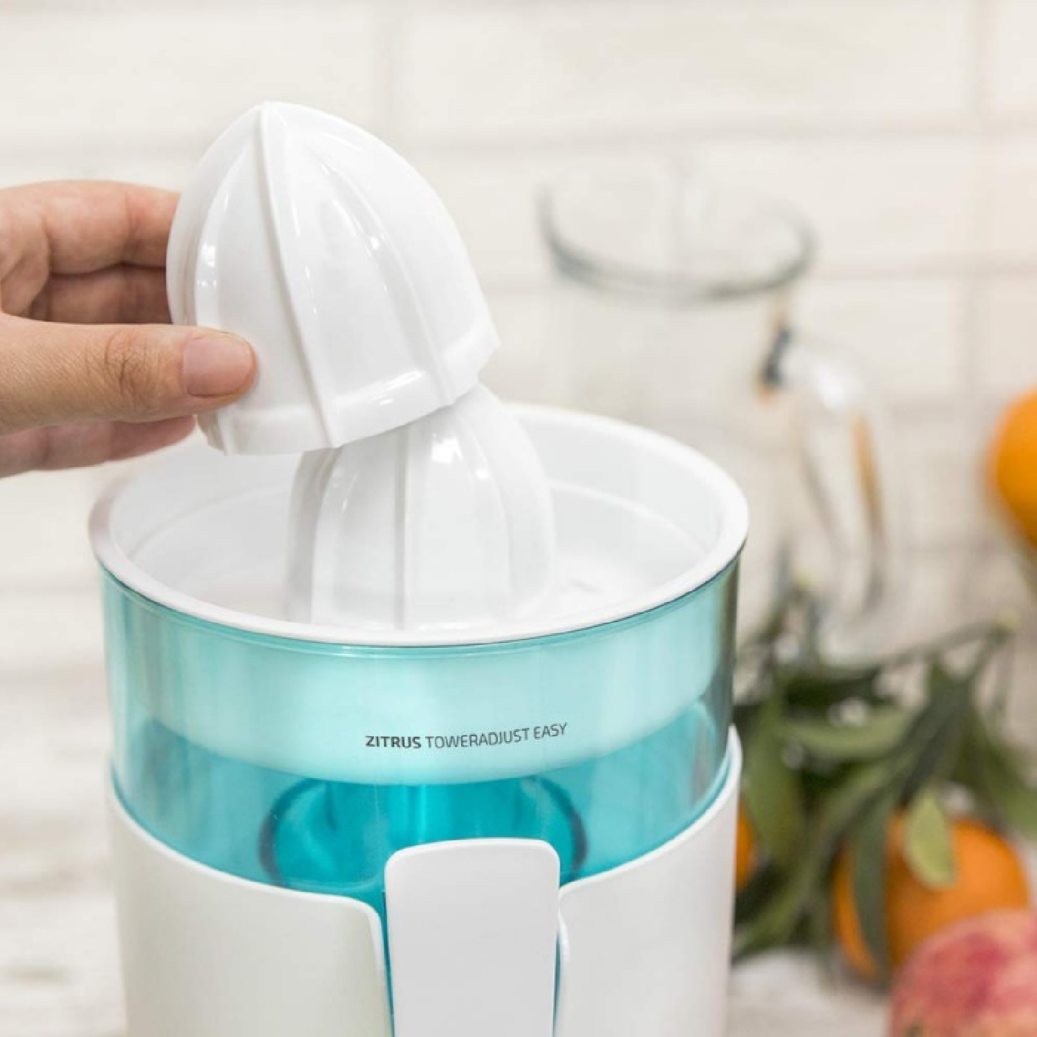 Mano inserisce il cono superiore di uno spremiagrumi bianco con serbatoio blu.