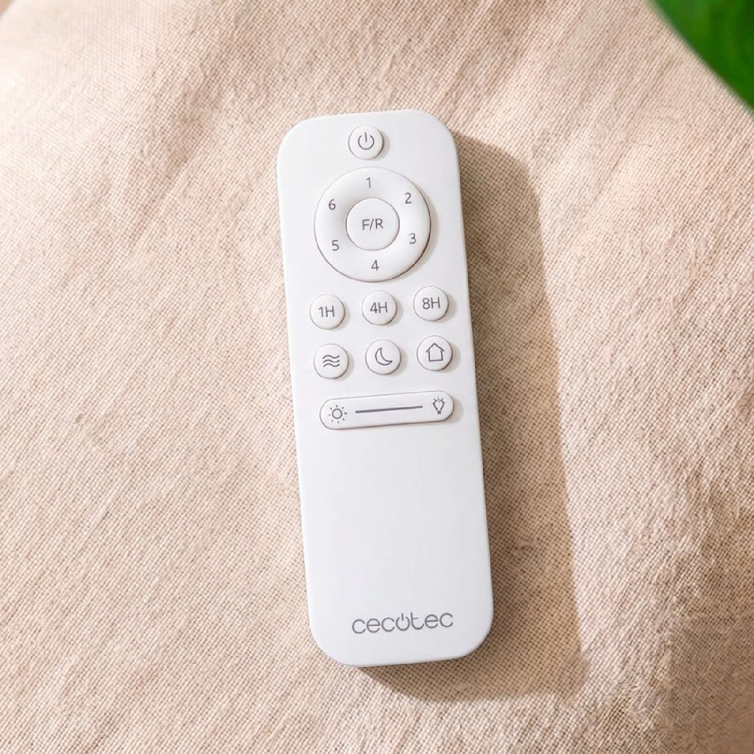 Un control remoto Cecotec blanco descansa sobre un fondo de tela beige texturizada.