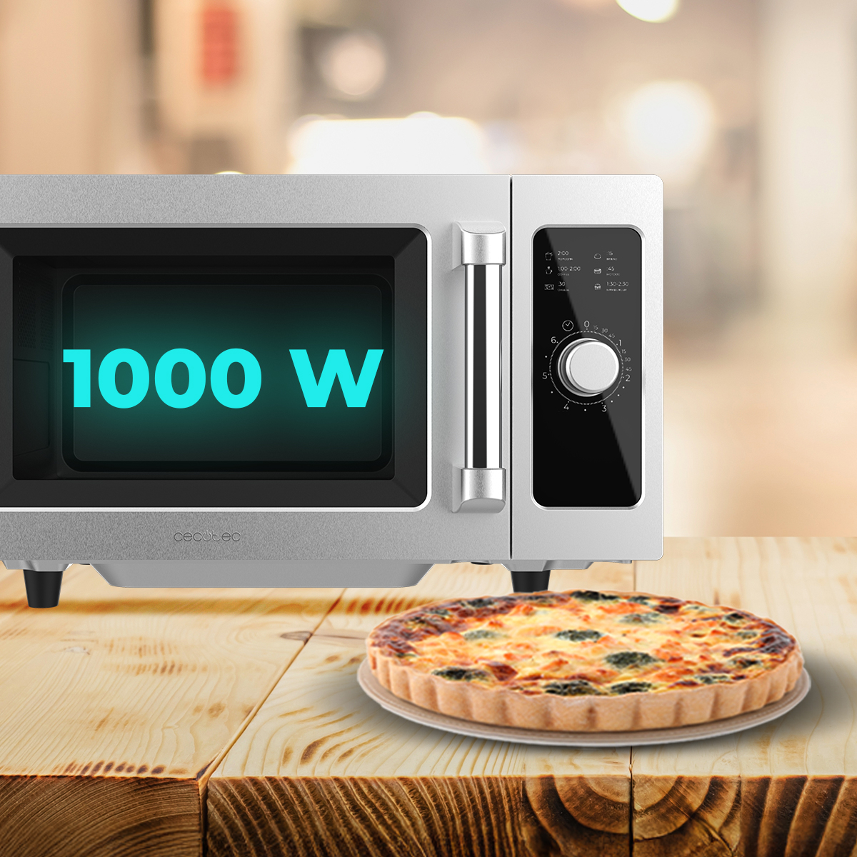 Un microondas plateado que muestra 1000 W en su pantalla descansa sobre una mesa de madera junto a una quiche.