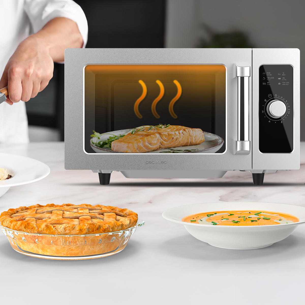 Un microondas plateado en un mostrador con pastel y sopa en primer plano.