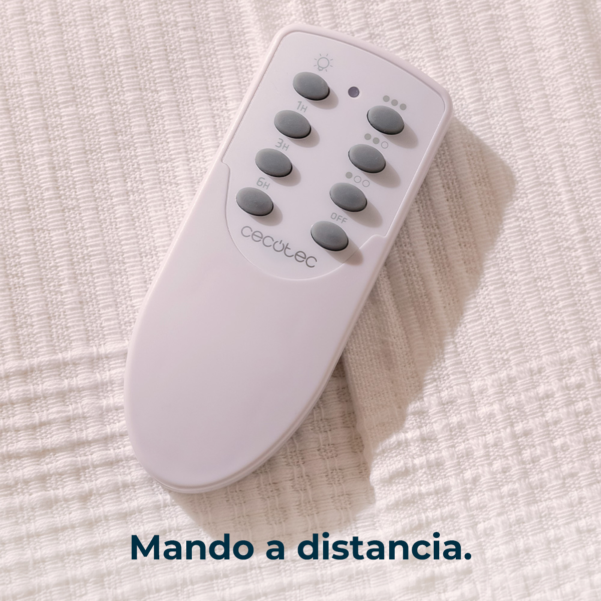 Un control remoto blanco Cecotec con botones grises sobre una manta beige texturizada.