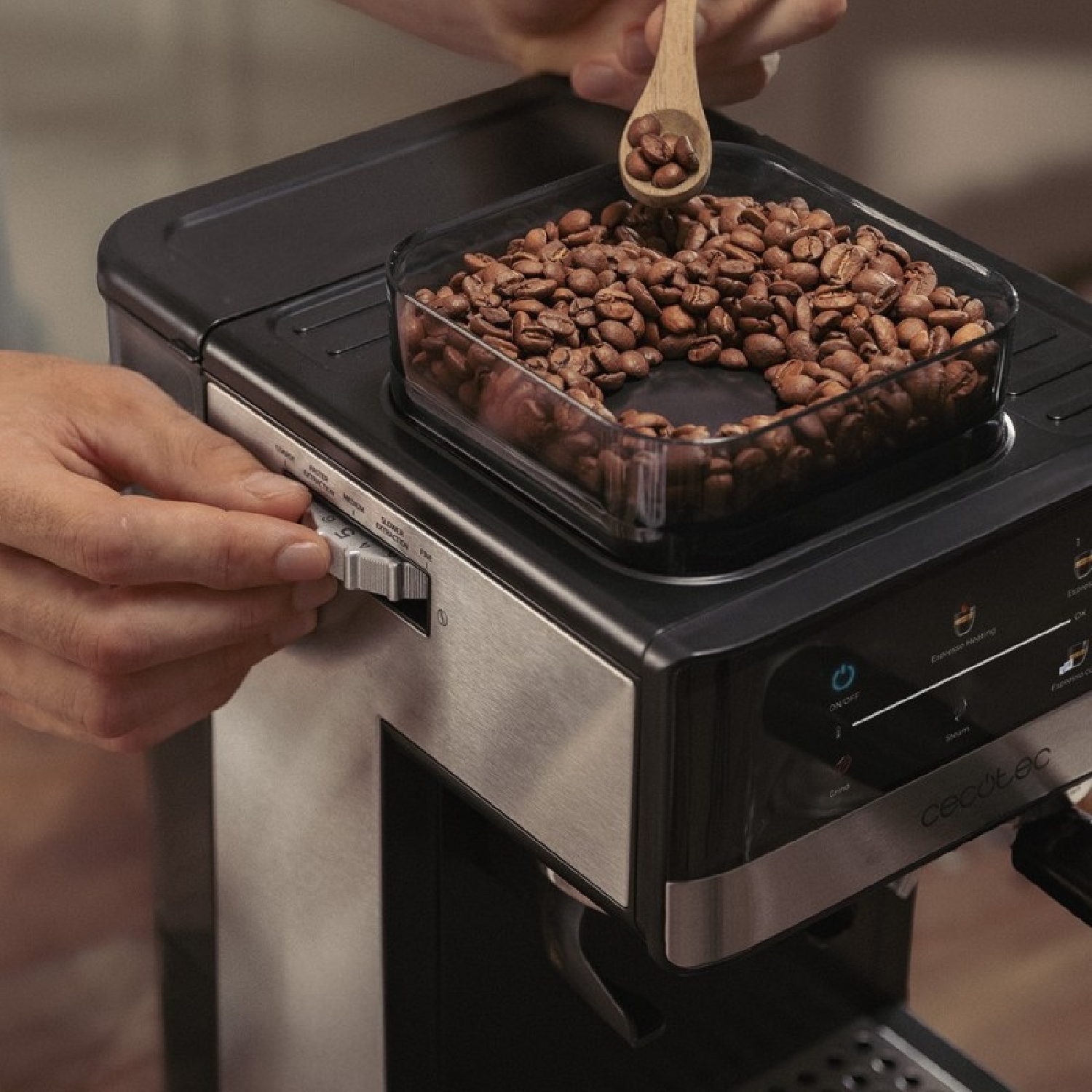 Una persona usa una cuchara de madera para añadir granos de café al molinillo de una cafetera negra.