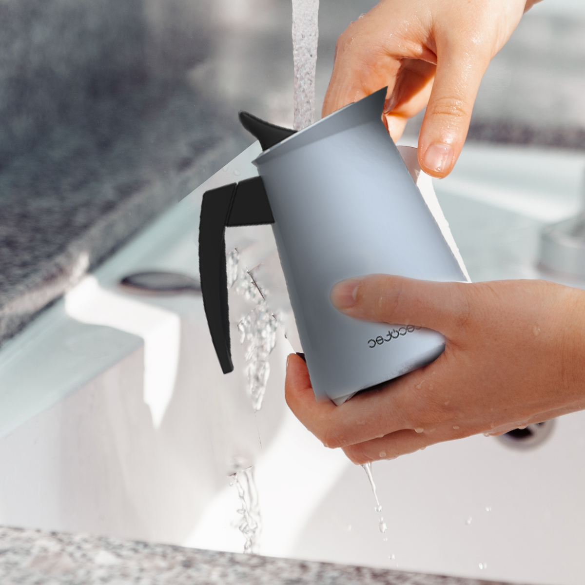 Mani che lavano una caffettiera grigia sotto l'acqua corrente in un lavandino.