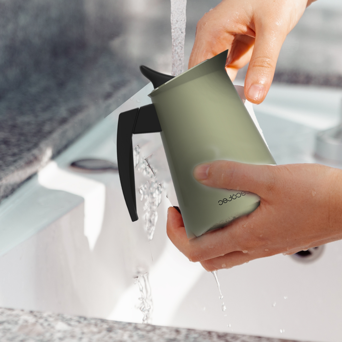 Mani che lavano una caffettiera verde chiaro con manico nero sotto l'acqua corrente in un lavandino.