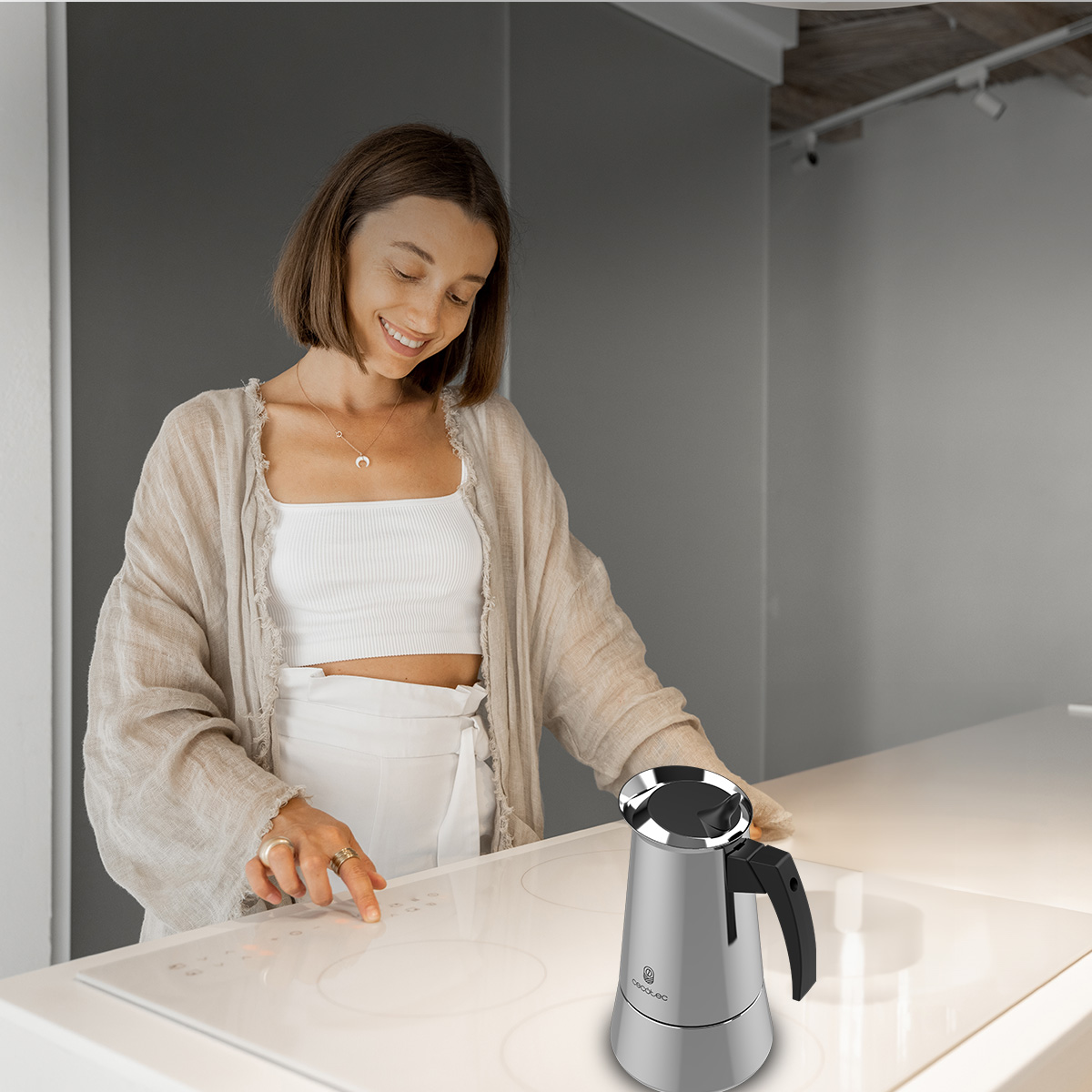 Una donna aziona un piano cottura a induzione bianco accanto a una caffettiera argentata.